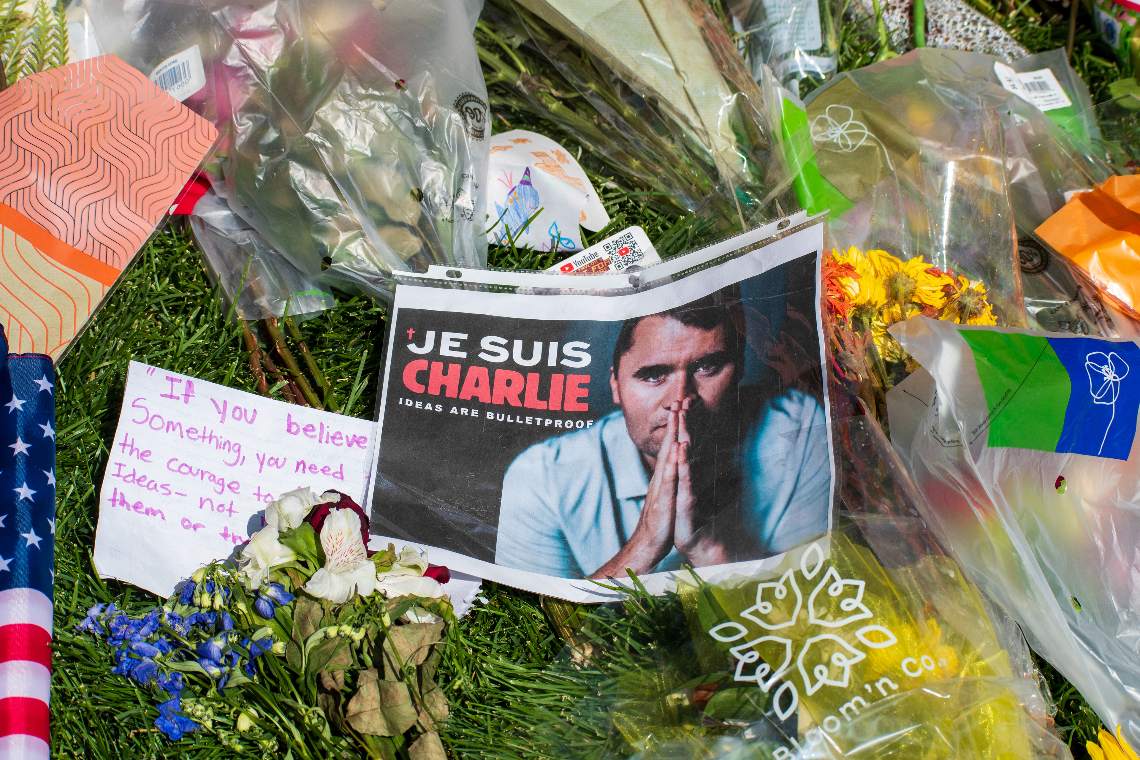 OREM, UTAH – SEPTEMBER 15, 2025: A printed image reading “JE SUIS CHARLIE” and “IDEAS ARE BULLETPROOF” is displayed at a memorial site for Charlie Kirk on the campus of Utah Valley University. The tribute includes bouquets of flowers, handwritten notes, and printed materials arranged on the grass. © Charles‑McClintock Wilson / ZUMA Press
