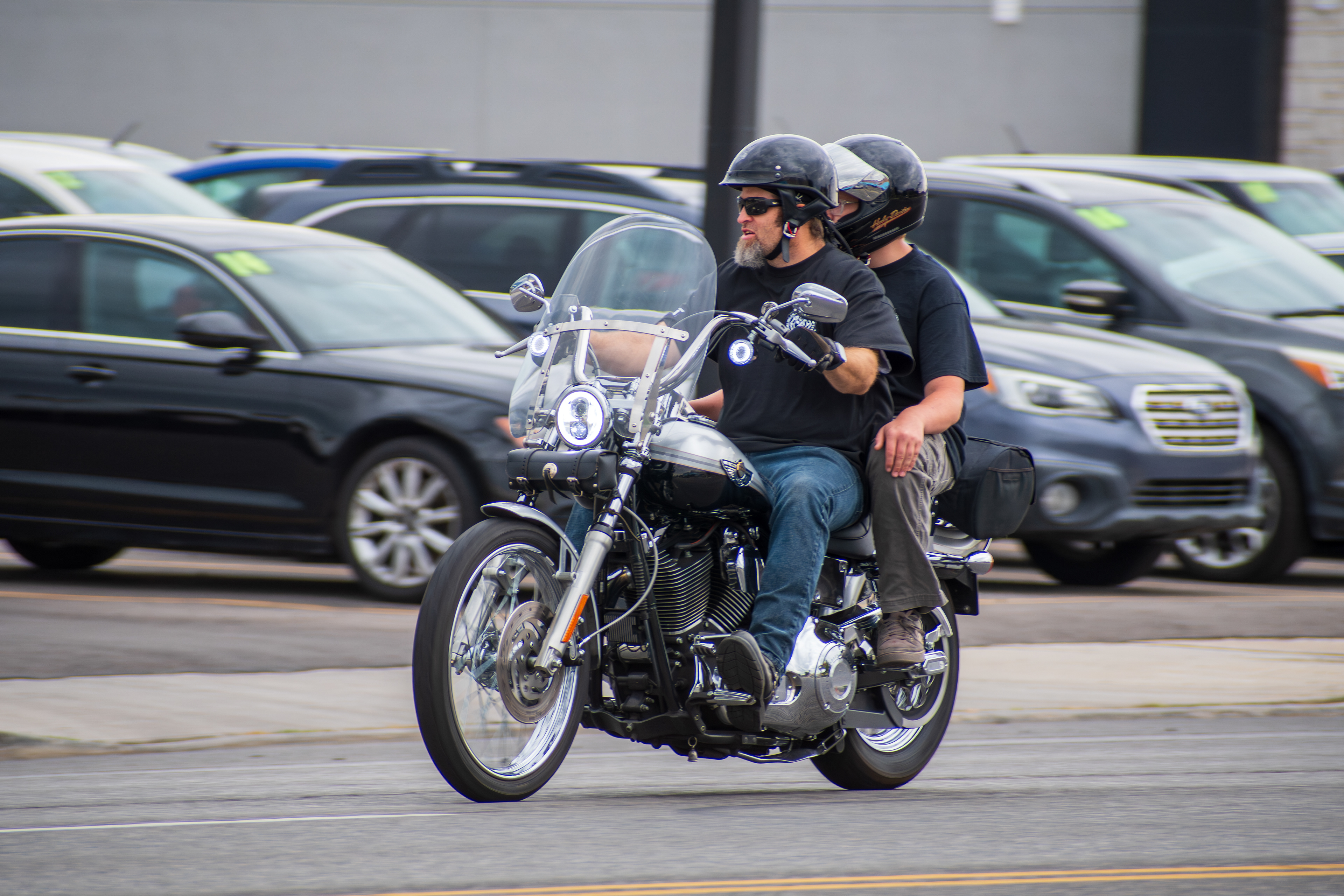 Murray, Utah — Sept. 8, 2025: A pair of riders cruise through downtown Murray on a cruiser-style motorcycle, framed by parked cars and midday shadows.