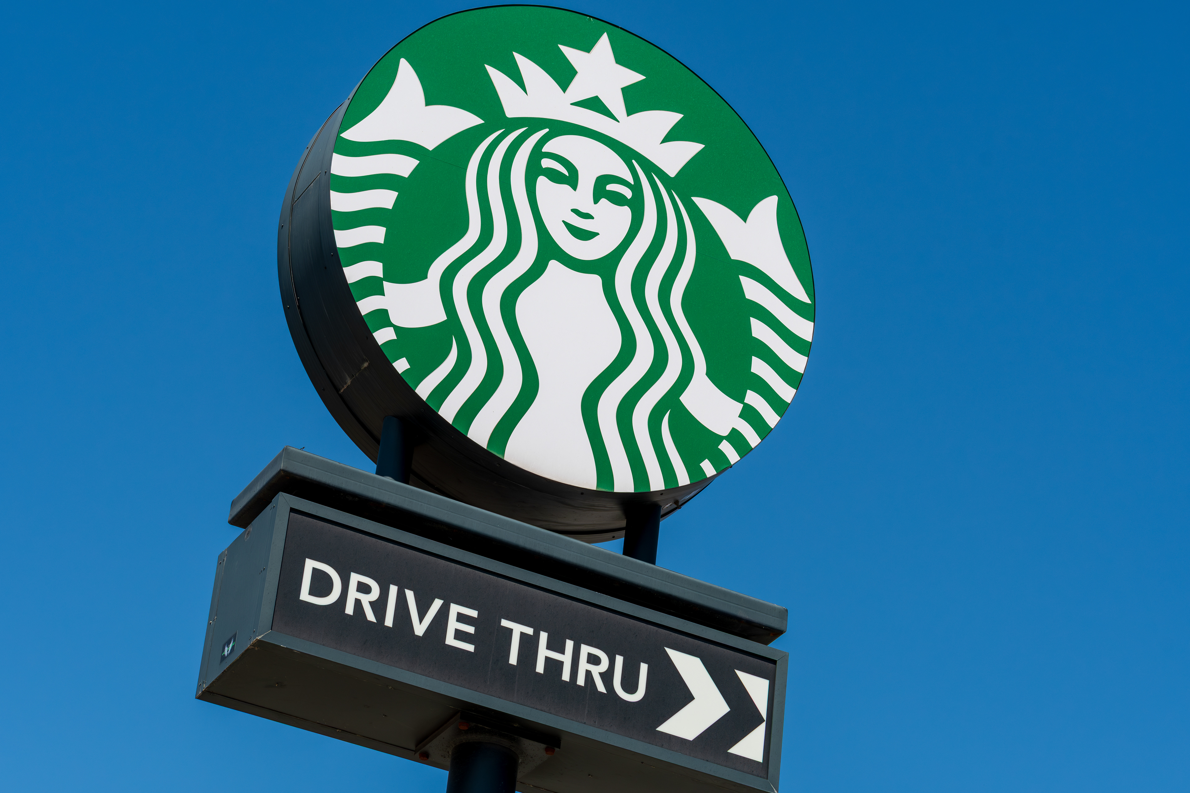 Provo, Utah, USA — September 1, 2025: A roadside Starbucks sign marks the drive-thru entrance, with a directional arrow guiding vehicles to the right.