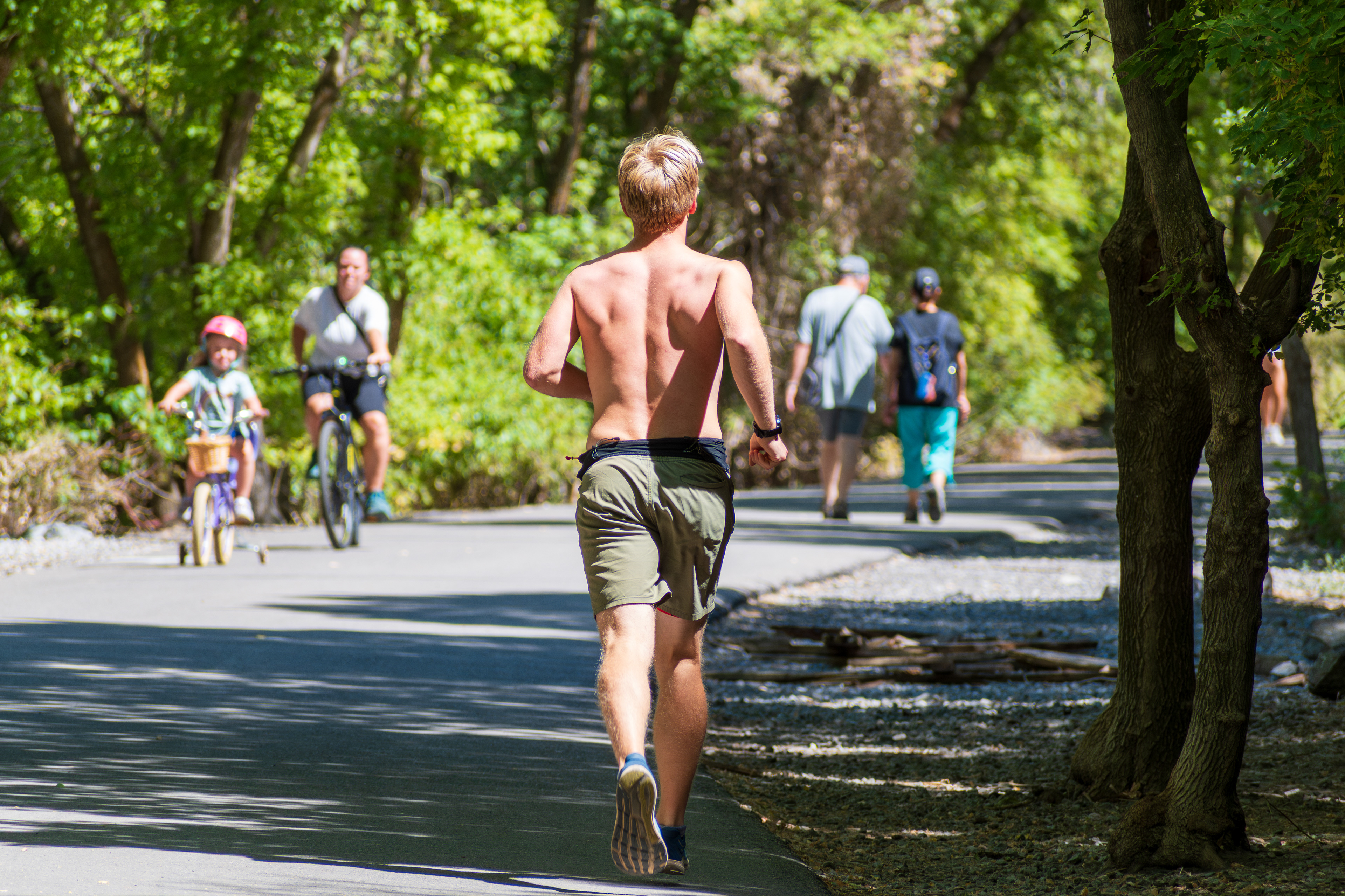 Provo Canyon, Utah, USA — September 1, 2025: A jogger runs along a wooded path as others walk and cycle in the background at Canyon Glen Park.