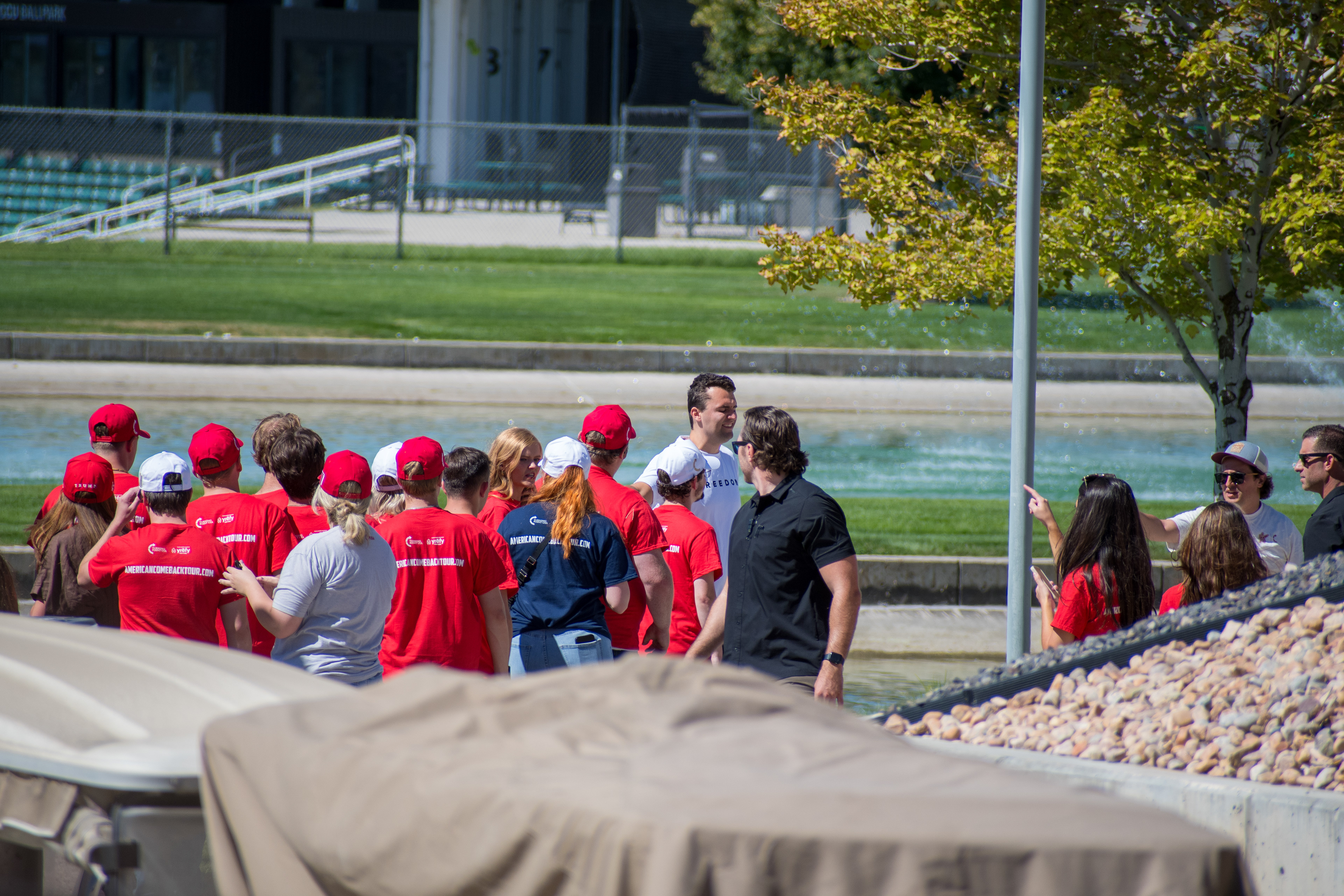OREM, UTAH – SEPTEMBER 10, 2025: Supporters gather near a water feature ahead of Charlie Kirk’s public appearance at Utah Valley University. Wearing red shirts and hats bearing political slogans, attendees stand near event infrastructure and vehicles in anticipation of Kirk’s arrival. The image reflects the branding, energy, and grassroots mobilization that shaped the atmosphere leading into his final public engagement. © Charles-McClintock Wilson / ZUMA Press