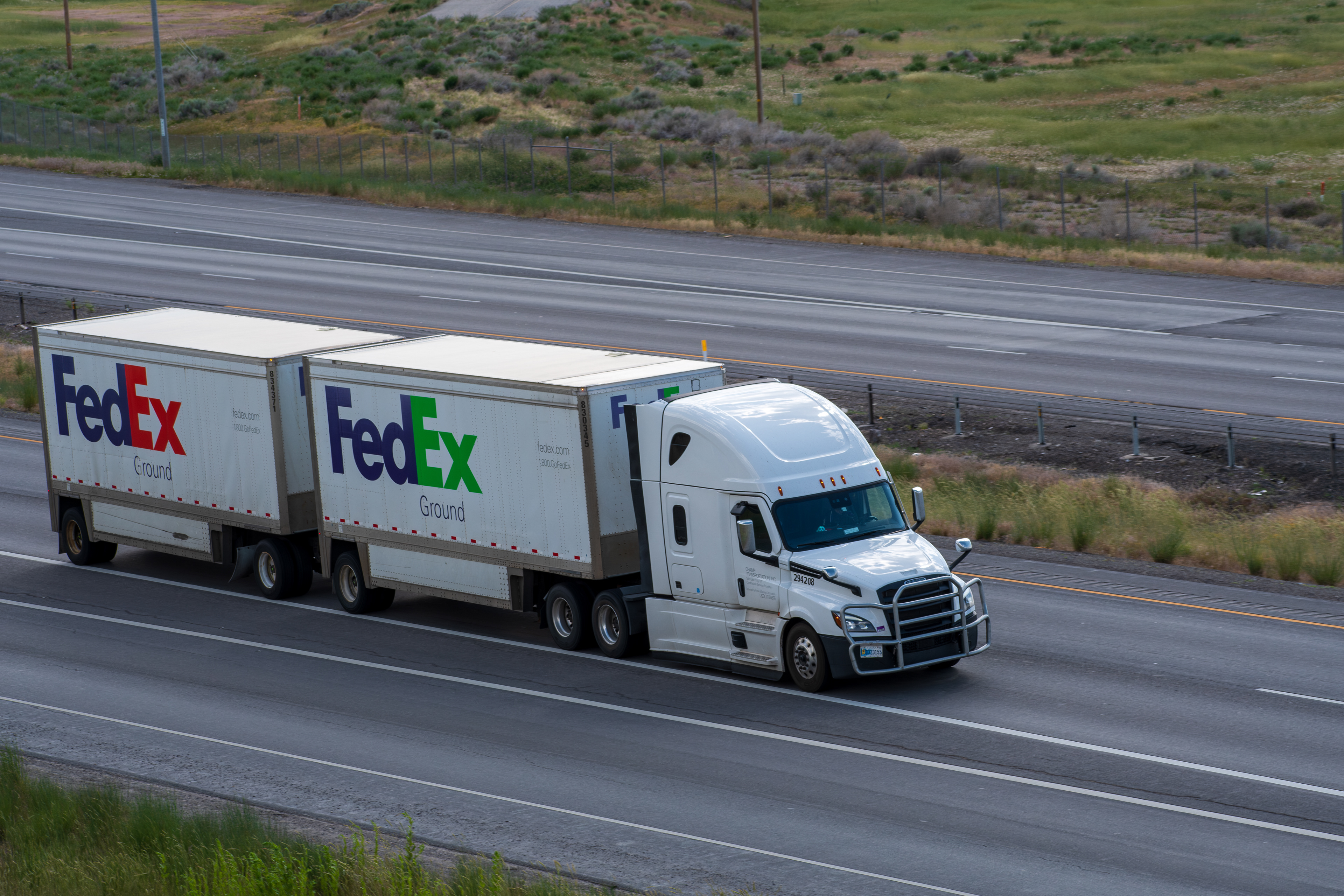 SANTAQUIN, UT – JUNE 8, 2025: FedEx truck travels on an empty I-15 carrying two containers—one branded FedEx Express, the other FedEx Ground. FedEx is a global courier delivery and logistics company.