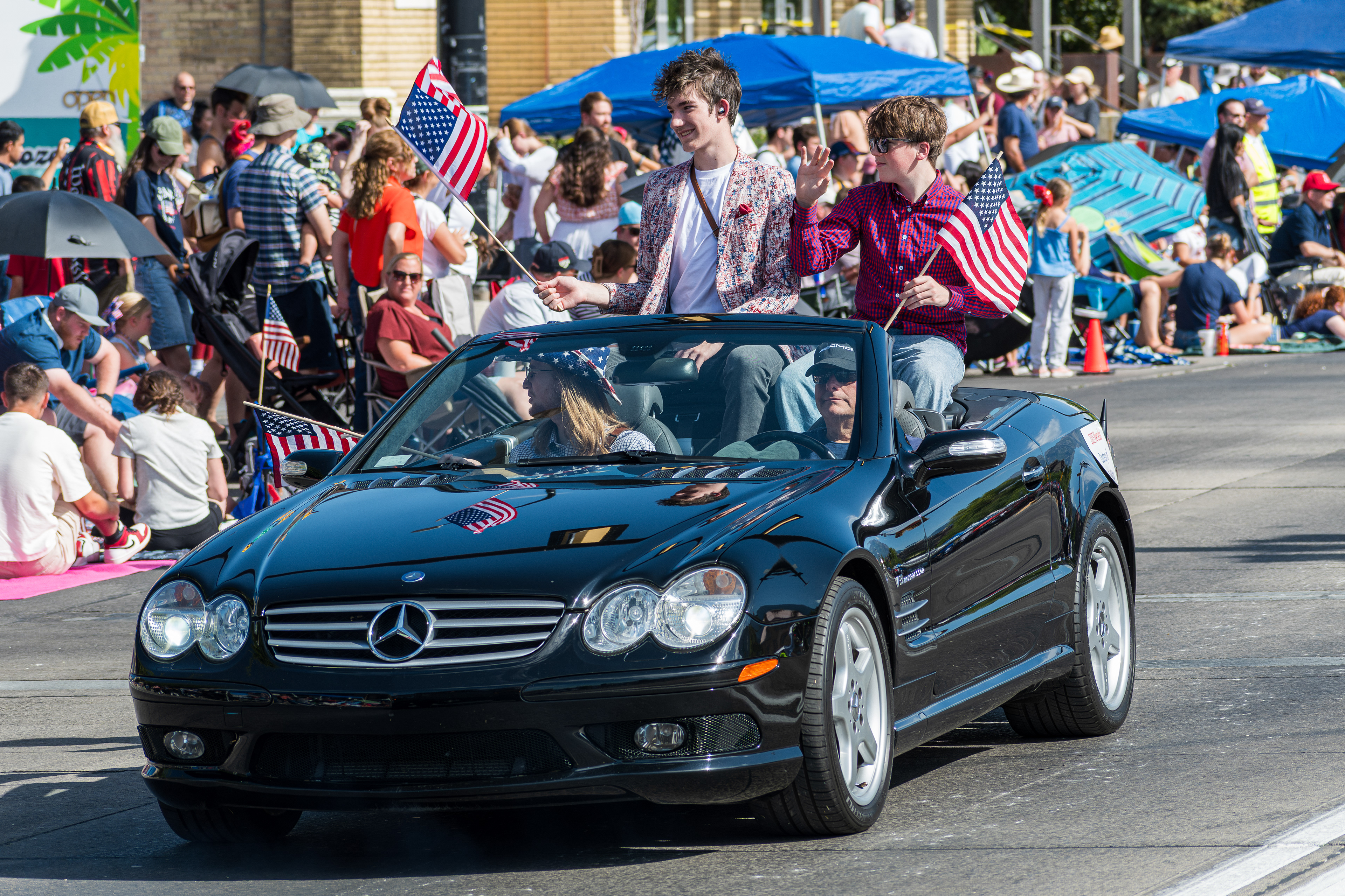 Provo, Utah – July 4, 2025: People holding American flags ride and wave from a Mercedes-Benz convertible during the Freedom Festival Grand Parade in downtown Provo.