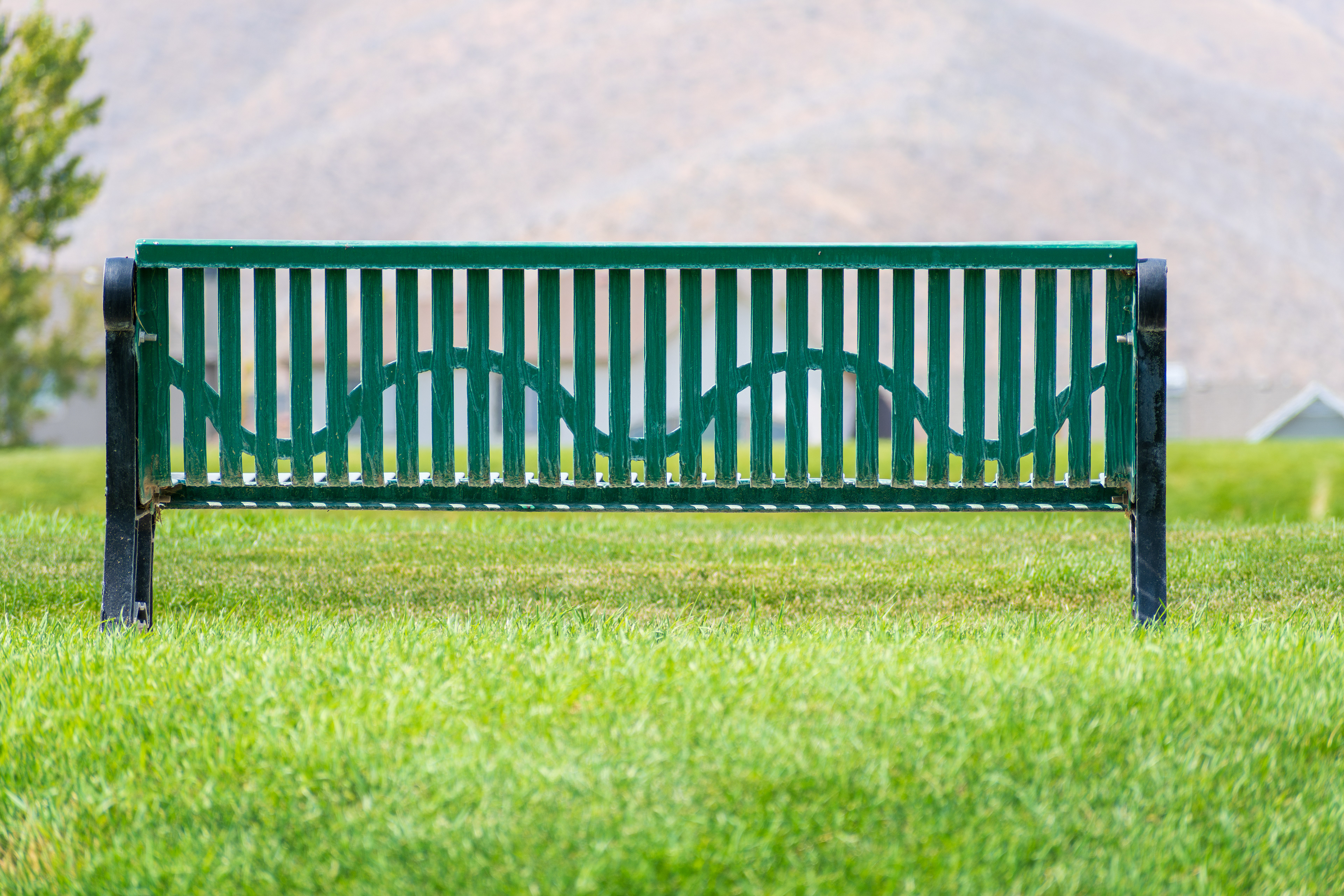 Salt Lake City, Utah, USA — September 1, 2025: A green metal park bench sits on a grassy area near a sidewalk with mountain terrain in the background.