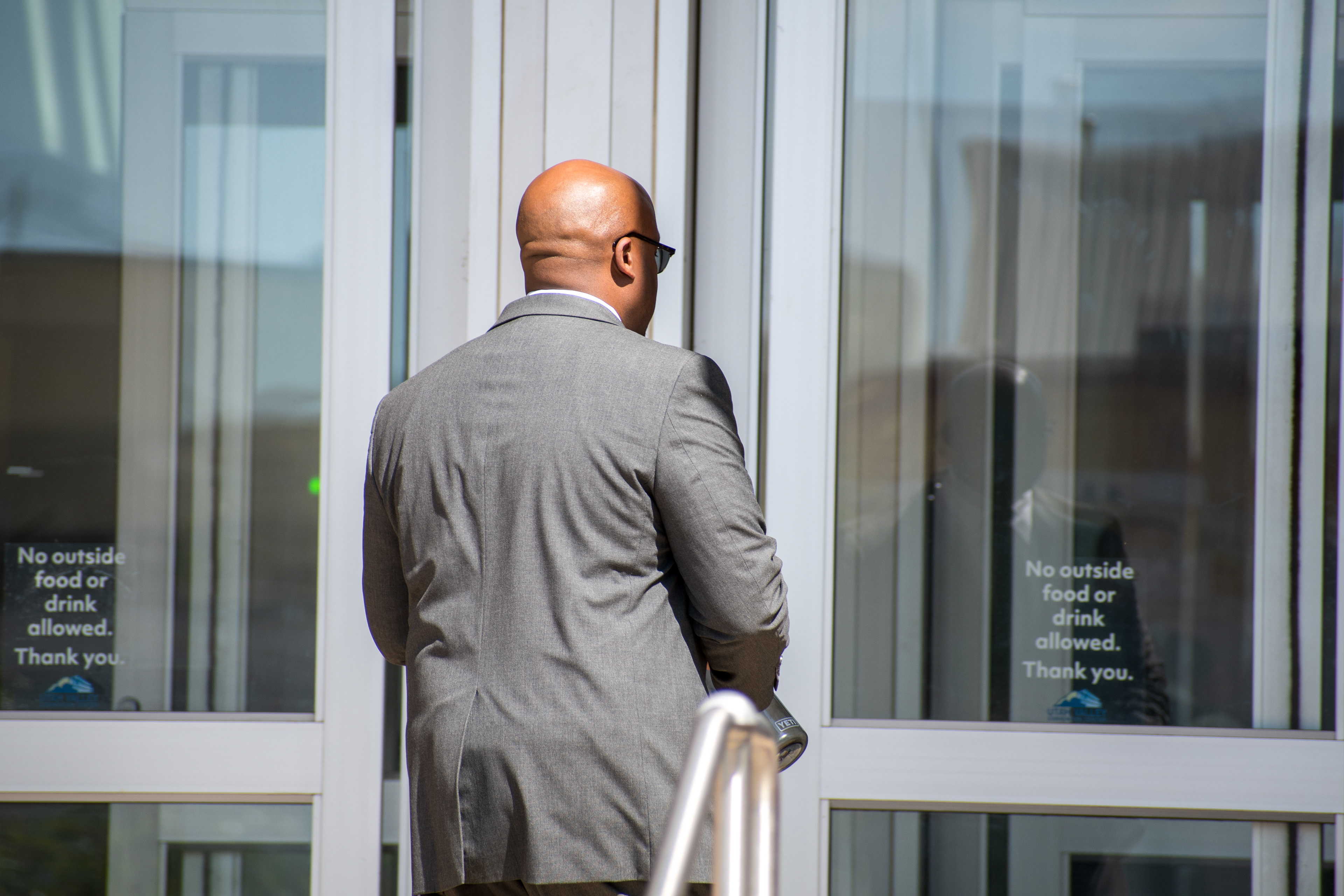 September 15, 2025 – Provo, Utah, United States: A man in a gray suit stands outside the Utah Valley Convention Center during the Department of Homeland Security career expo. Signs posted on the glass doors outline event regulations as attendees arrive amid heightened security and public protest. Photograph by Charles‑McClintock Wilson / ZUMA Press Wire