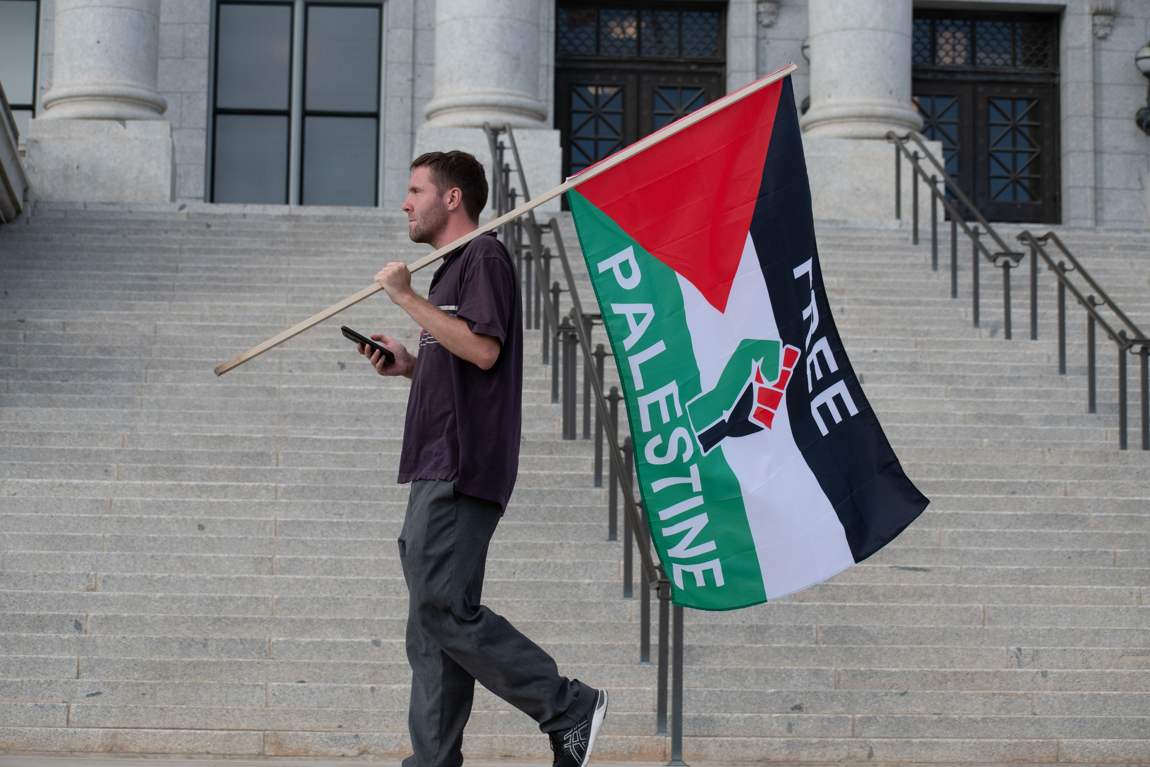 October 10, 2025, Salt Lake City, Utah, USA: A demonstrator walks up the steps of the Utah State Capitol during the Free Palestine Rally. The participant holds a flag featuring symbolic imagery and bold colors while using a smartphone. (Credit Image: © Charles-McClintock Wilson/ZUMA Press Wire)