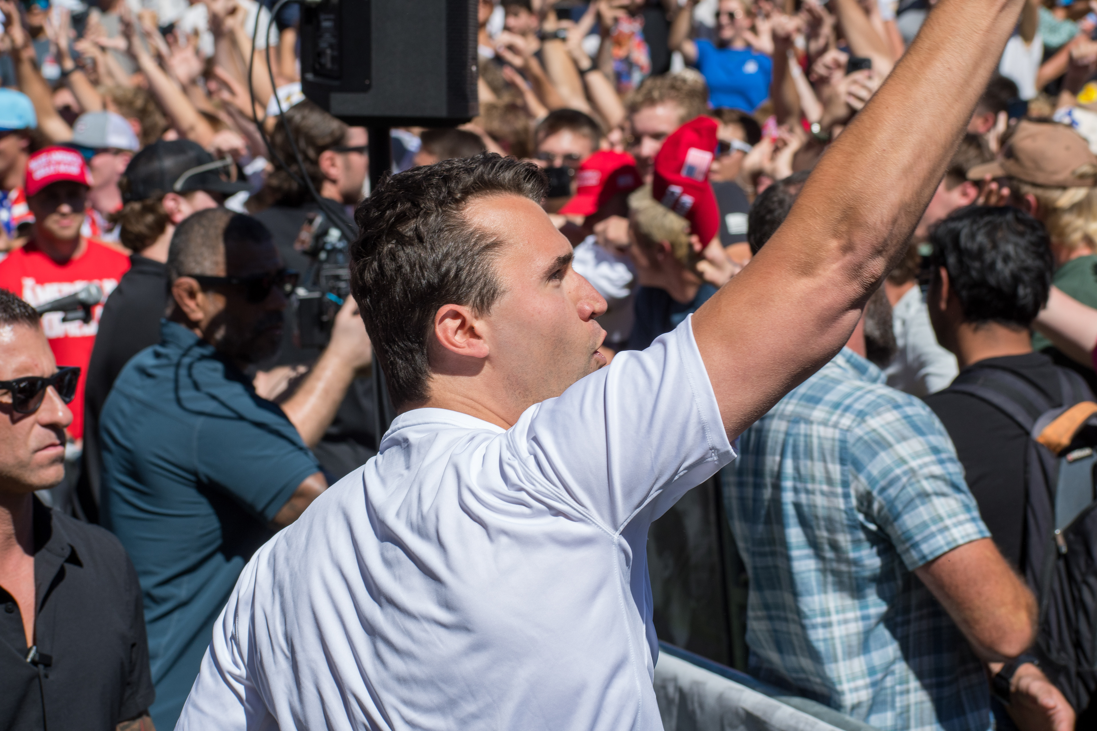Charlie Kirk stands before a crowd of supporters during a public event at Utah Valley University. Separated by metal barricades, attendees raise phones and cheer as Kirk addresses them in one of his final public moments. The image reflects the intensity of civic engagement and the charged atmosphere that defined the gathering. © Charles-McClintock Wilson / ZUMA Press