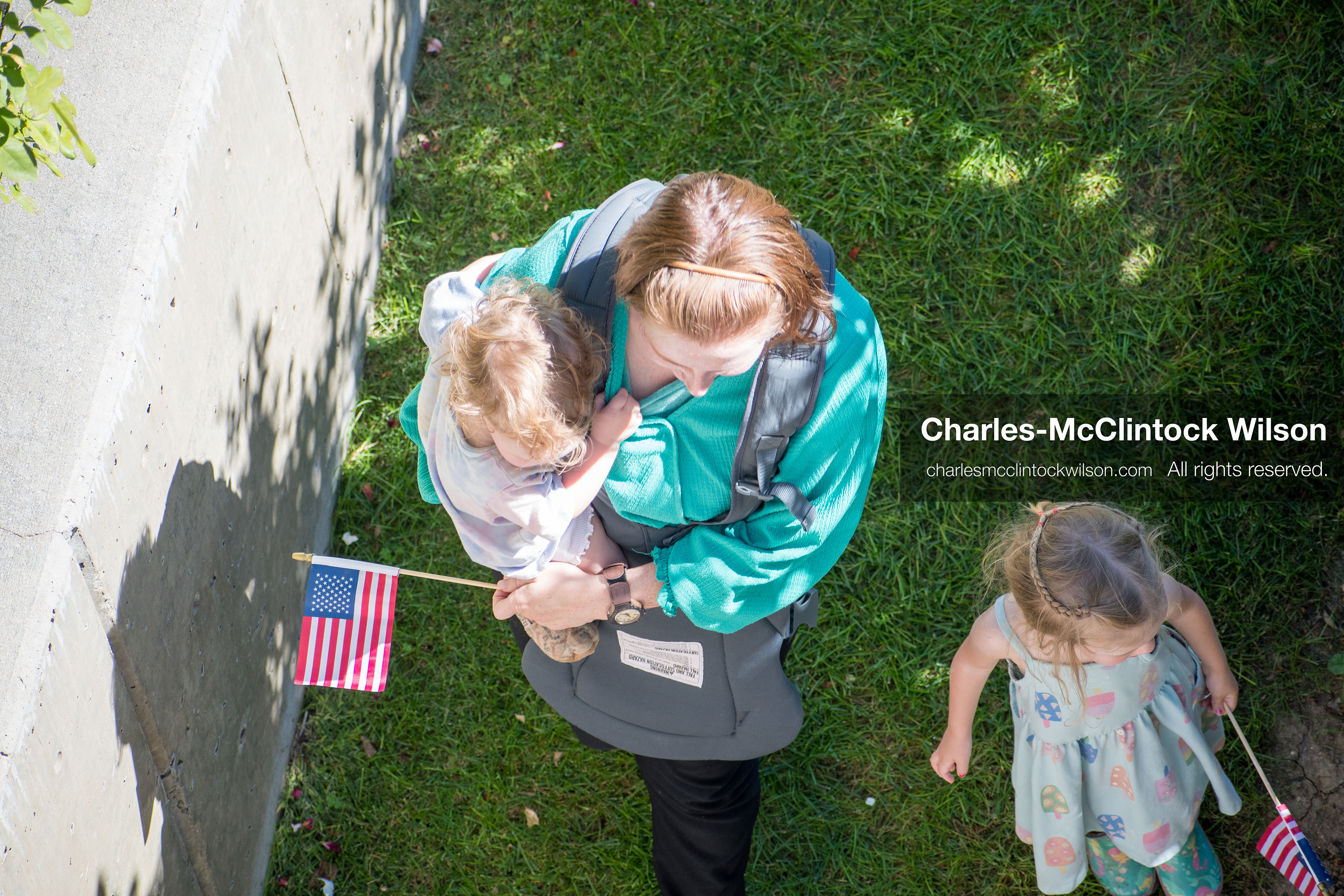 September 10, 2025, Orem, Utah, USA: A parent carries a child in a front-facing carrier while another child stands nearby, both holding small American flags during conservative activist Charlie Kirk’s American Comeback Tour appearance at Utah Valley University. The event, held at the Fountain Courtyard, drew over 3,000 attendees and was marked by civic tension and symbolic gestures from across the political spectrum. Kirk was fatally shot moments later during the public Q&A session, prompting national scrutiny of campus security protocols. (Credit Image: © Charles‑McClintock Wilson/All rights reserved)