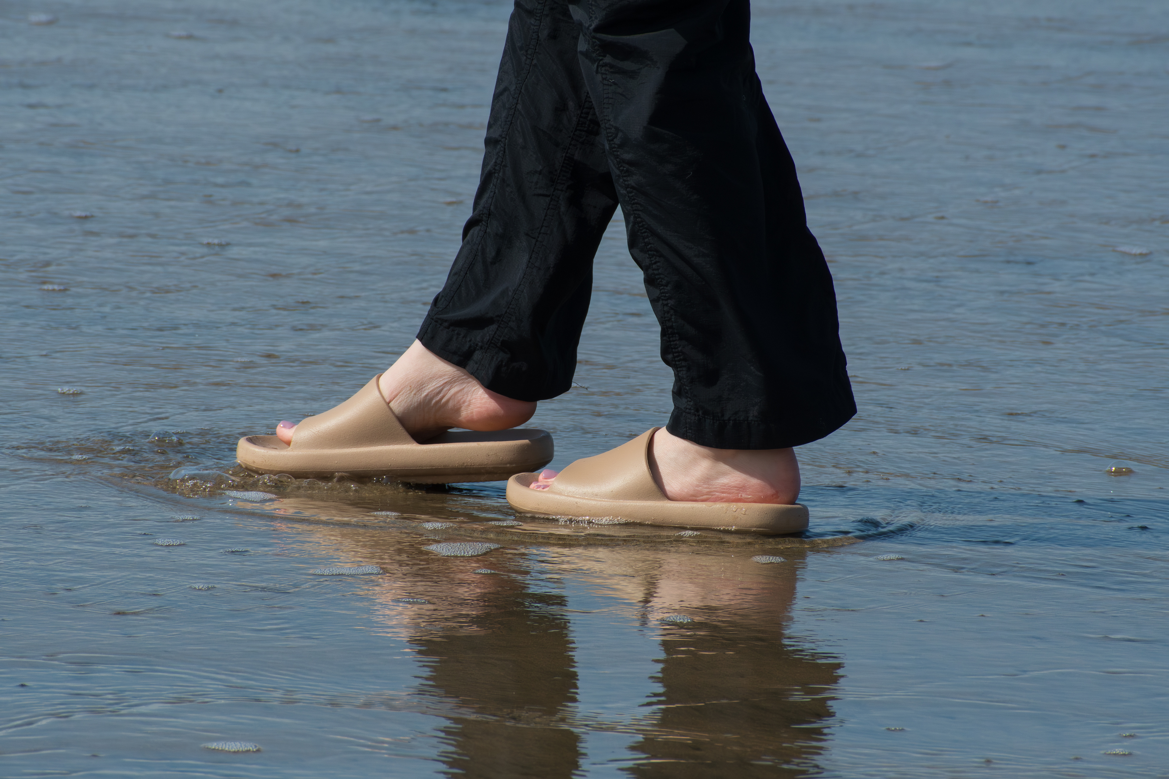  CANNON BEACH, OR, USA - APR 12, 2025: A close-up of a woman's feet in slide sandals on the sandy shores of Cannon Beach, capturing a serene moment along the Oregon coastline