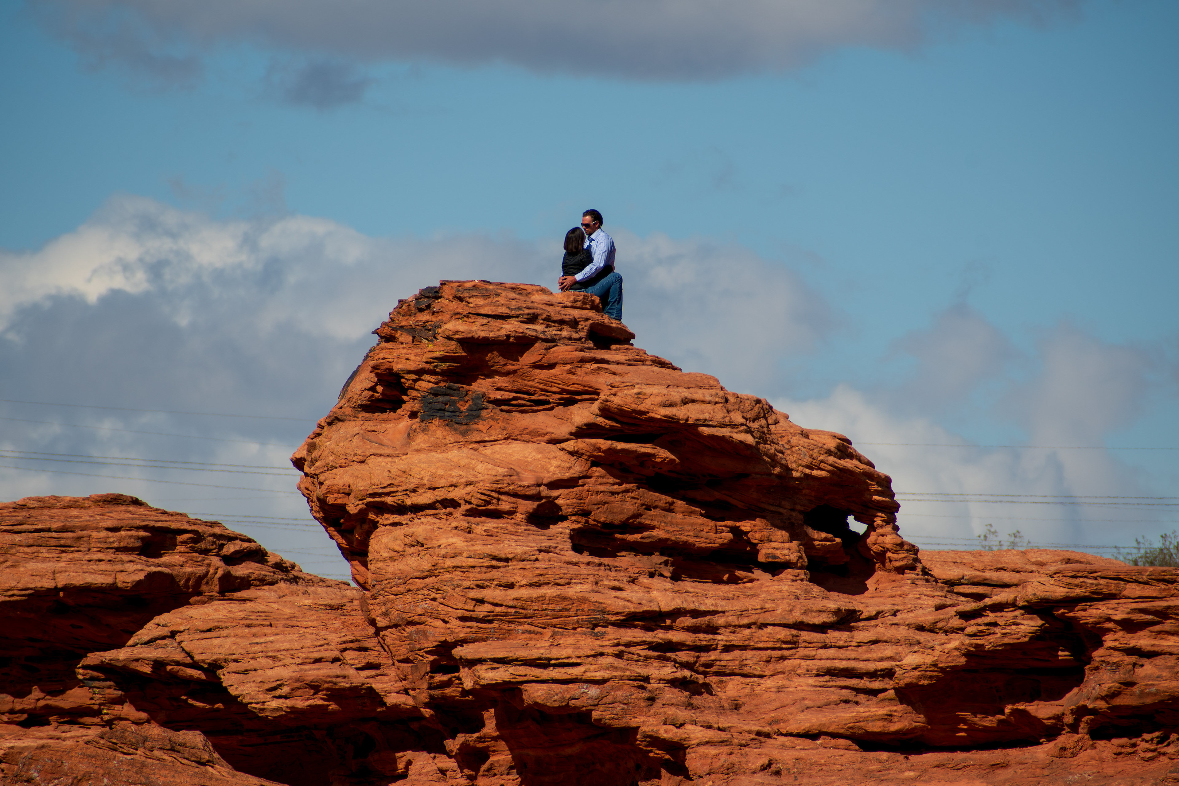 ST. GEORGE, UT - MAY 10: A couple sits atop a red sandstone formation at Pioneer Park in St. George, Utah, on May 10, 2025. Known for its sweeping views and unique geological features, the 52-acre park includes natural arches, narrow slot canyons, and the iconic Dixie Rock, making it a popular destination for both locals and tourists.