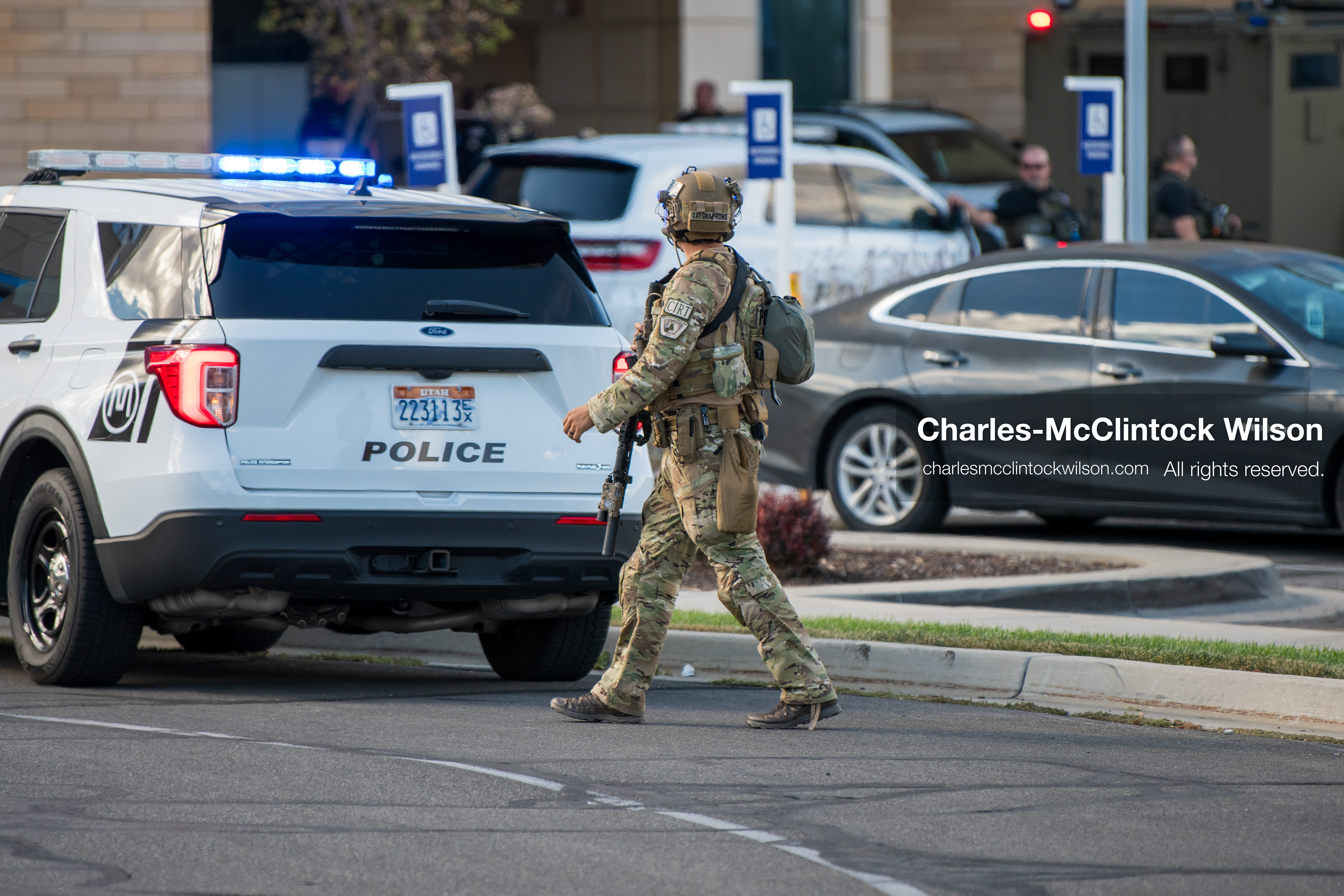 An armed law enforcement officer wearing camouflage tactical gear and a helmet patrols a roadway checkpoint outside Intermountain Medical Center in Murray, Utah, United States, on August 17, 2026. Multiple regional police agencies secured the hospital perimeter as a safety precaution after shooting victims were admitted following a fatal shootout outside a funeral service in nearby Kearns. (Photo by Charles-McClintock Wilson/NurPhoto)