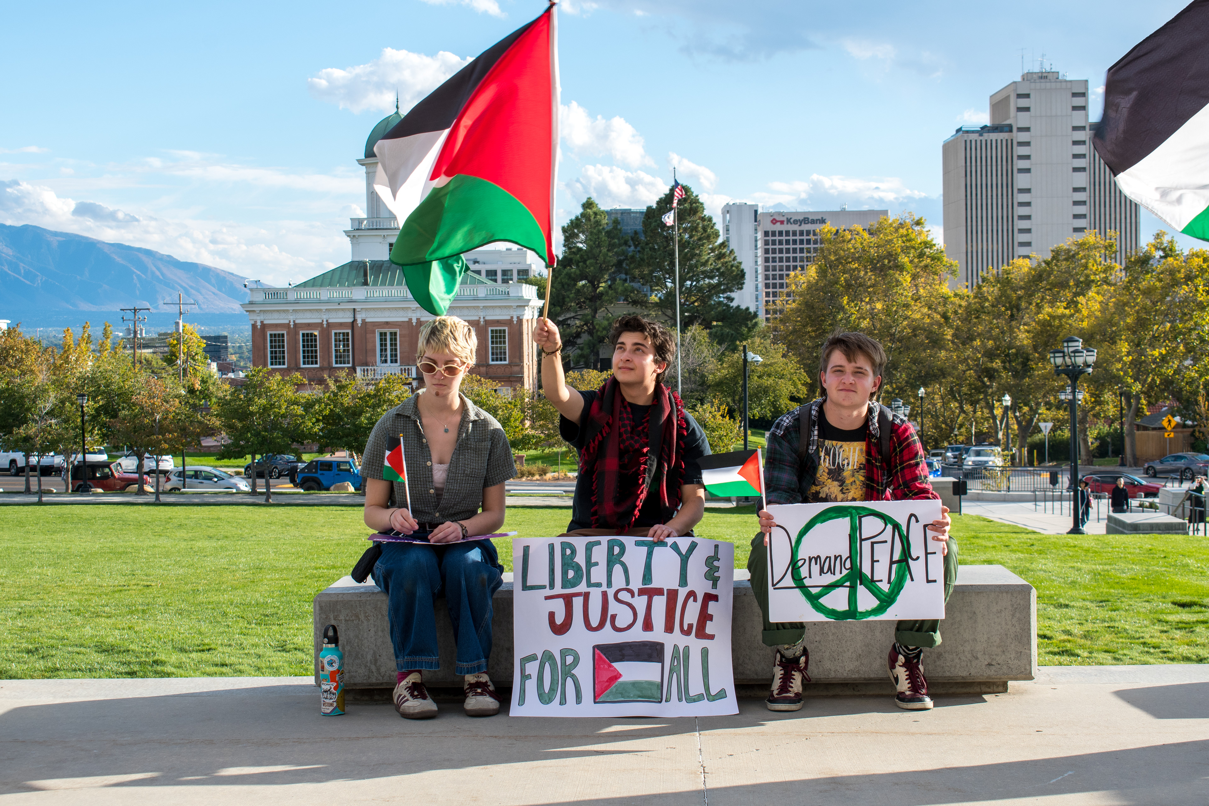 October 10, 2025, Salt Lake City, Utah, USA: Demonstrators sit on a concrete bench during the Free Palestine Rally organized in front of the Utah State Capitol. Participants display flags and signs as city buildings and mountain peaks frame the background. (Credit Image: © Charles-McClintock Wilson/ZUMA Press Wire)