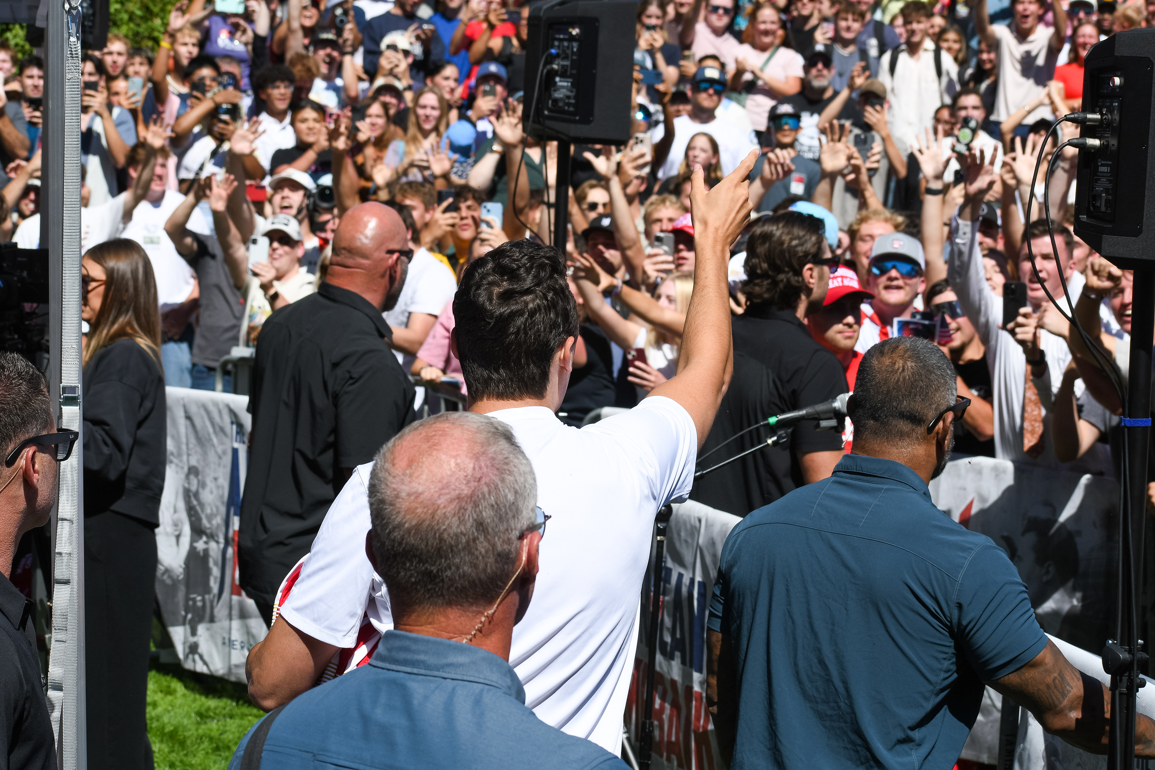 Charlie Kirk stands before a crowd of supporters during a public event at Utah Valley University. Separated by metal barricades, attendees raise phones and cheer as Kirk addresses them in one of his final public moments. The image reflects the intensity of civic engagement and the charged atmosphere that defined the gathering. © Charles-McClintock Wilson / ZUMA Press