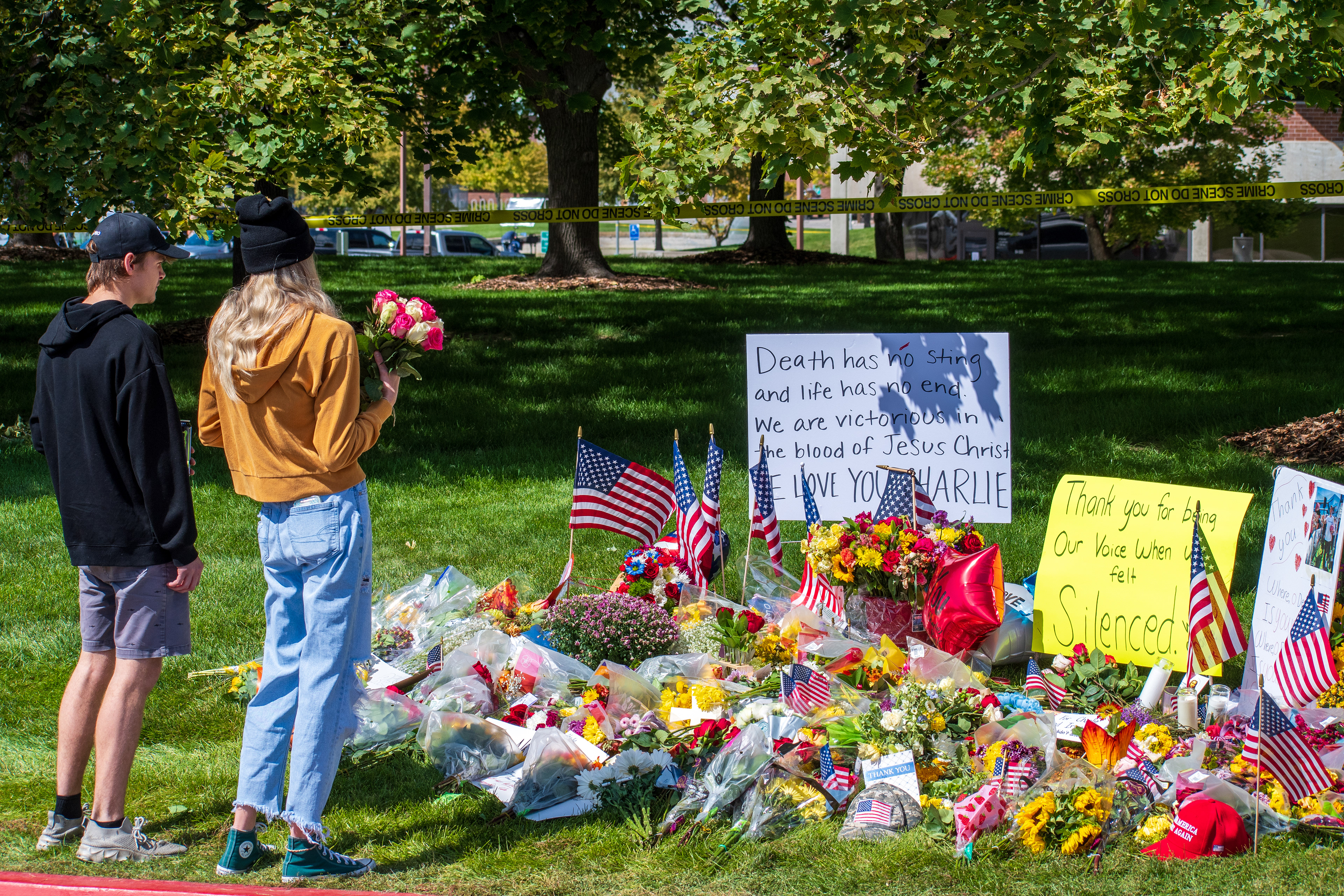 OREM, UTAH – SEPTEMBER 12, 2025: Two mourners stand before a memorial site for Charlie Kirk near Utah Valley University, one holding a bouquet of flowers. Surrounded by candles, stuffed animals, handwritten posters, and American flags, the tribute reflects a moment of solemn remembrance. © Charles‑McClintock Wilson / ZUMA Press