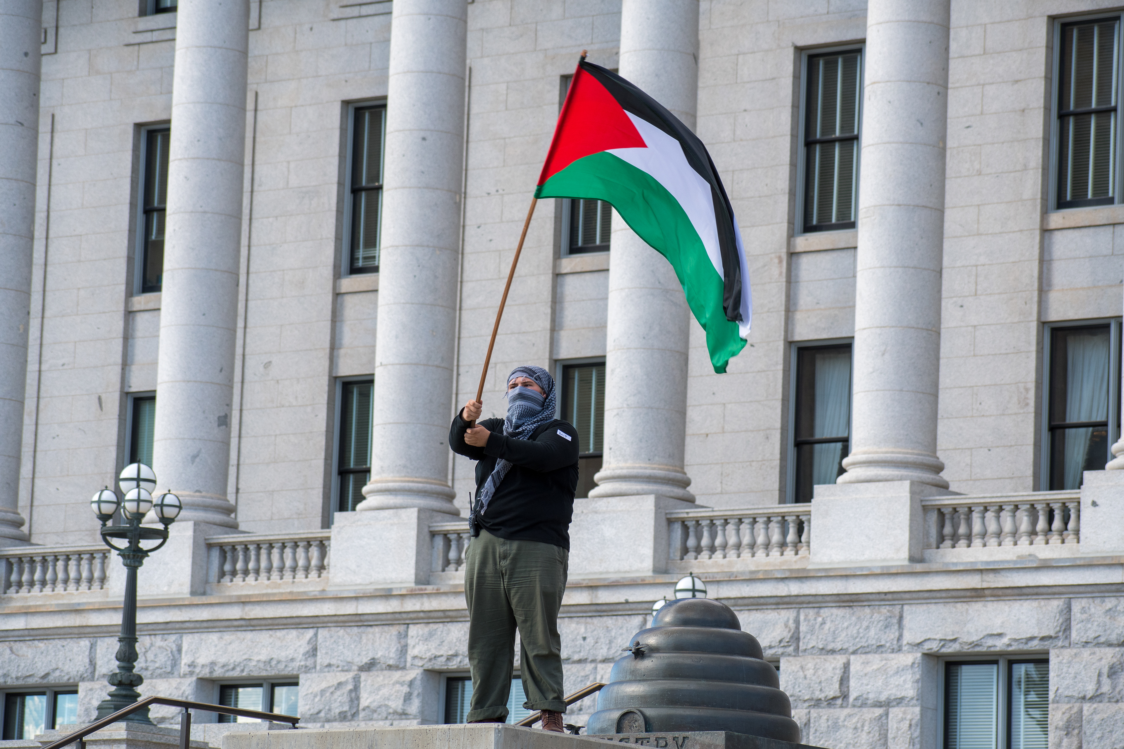 October 10, 2025, Salt Lake City, Utah, USA: A demonstrator stands on a raised platform outside the Utah State Capitol during the Free Palestine Rally. The participant waves a Palestinian flag while wearing a face covering and casual clothing. (Credit Image: © Charles-McClintock Wilson/ZUMA Press Wire)