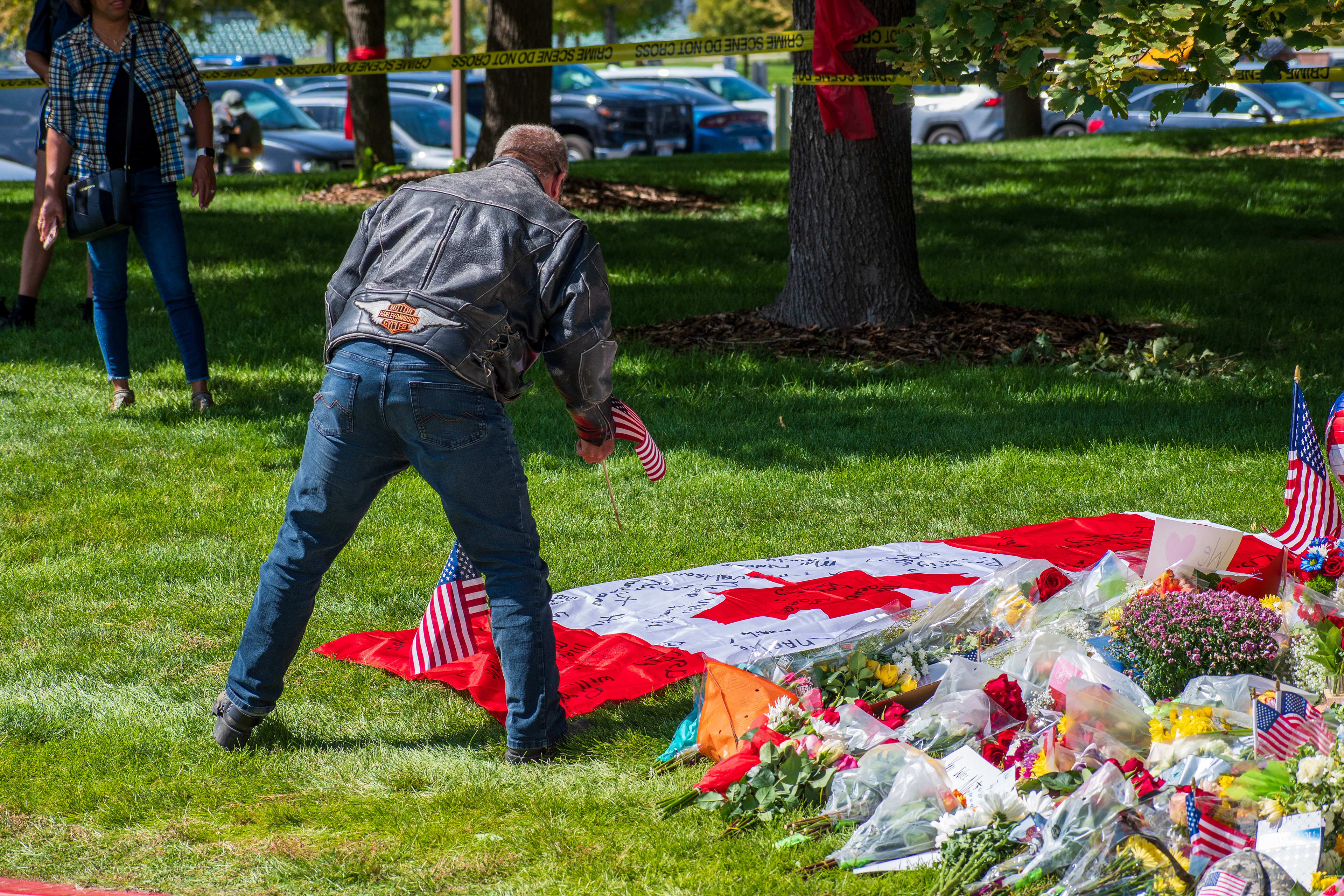 OREM, UTAH – SEPTEMBER 12, 2025: A man places small American flags beside a Canadian flag laid out on the grass at a memorial site for Charlie Kirk near Utah Valley University. Flowers and tribute items surround the display as people gather in the background. © Charles‑McClintock Wilson / ZUMA Press