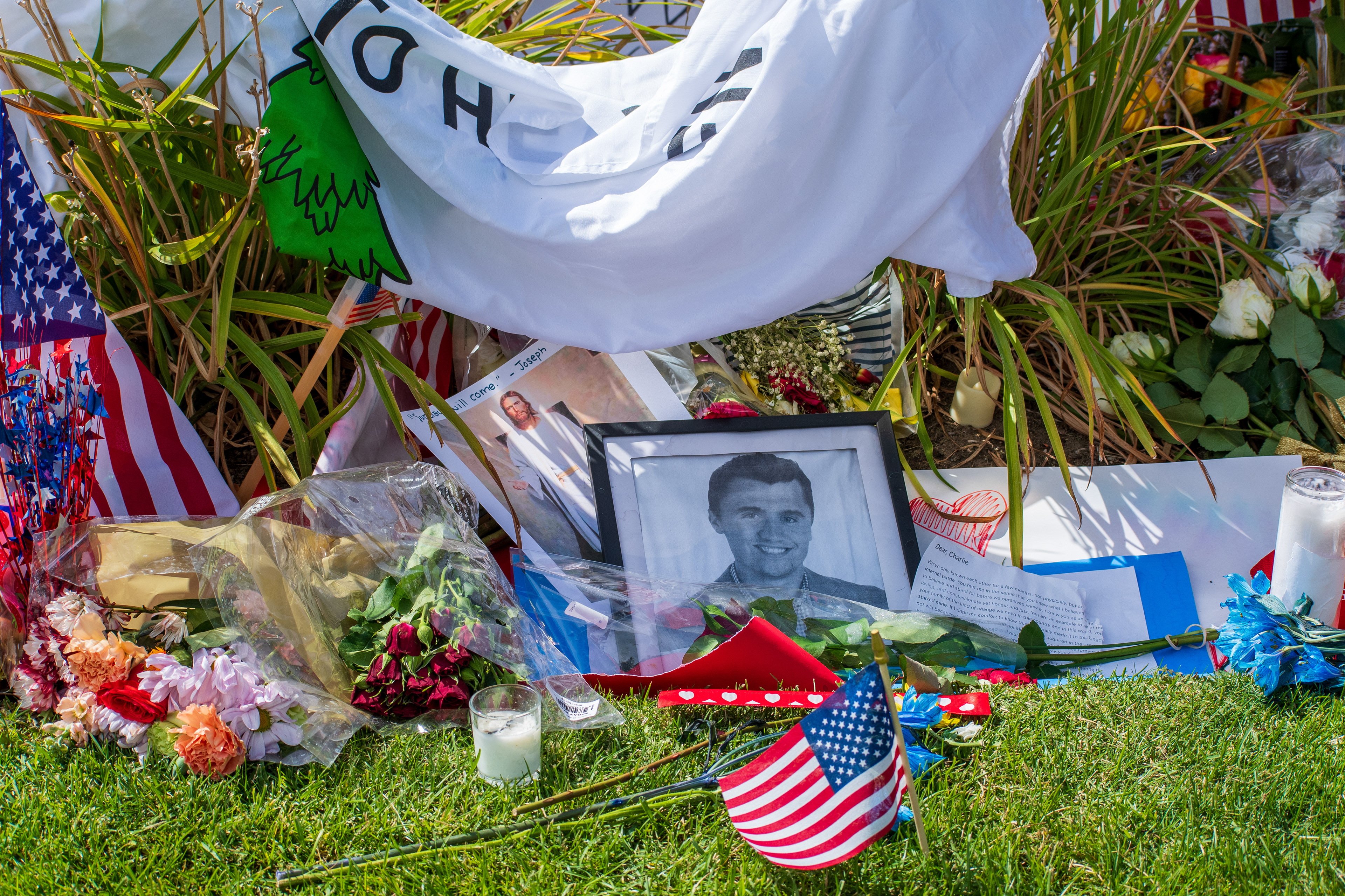 OREM, UTAH – SEPTEMBER 12, 2025: A framed black-and-white photograph is surrounded by American flags, flowers, handwritten notes, and personal tributes at a memorial site for Charlie Kirk outside Timpanogos Regional Hospital. Red and white roses, a bouquet wrapped in plastic, and a white cloth with green and red designs are arranged around the image. © Charles‑McClintock Wilson / ZUMA Press