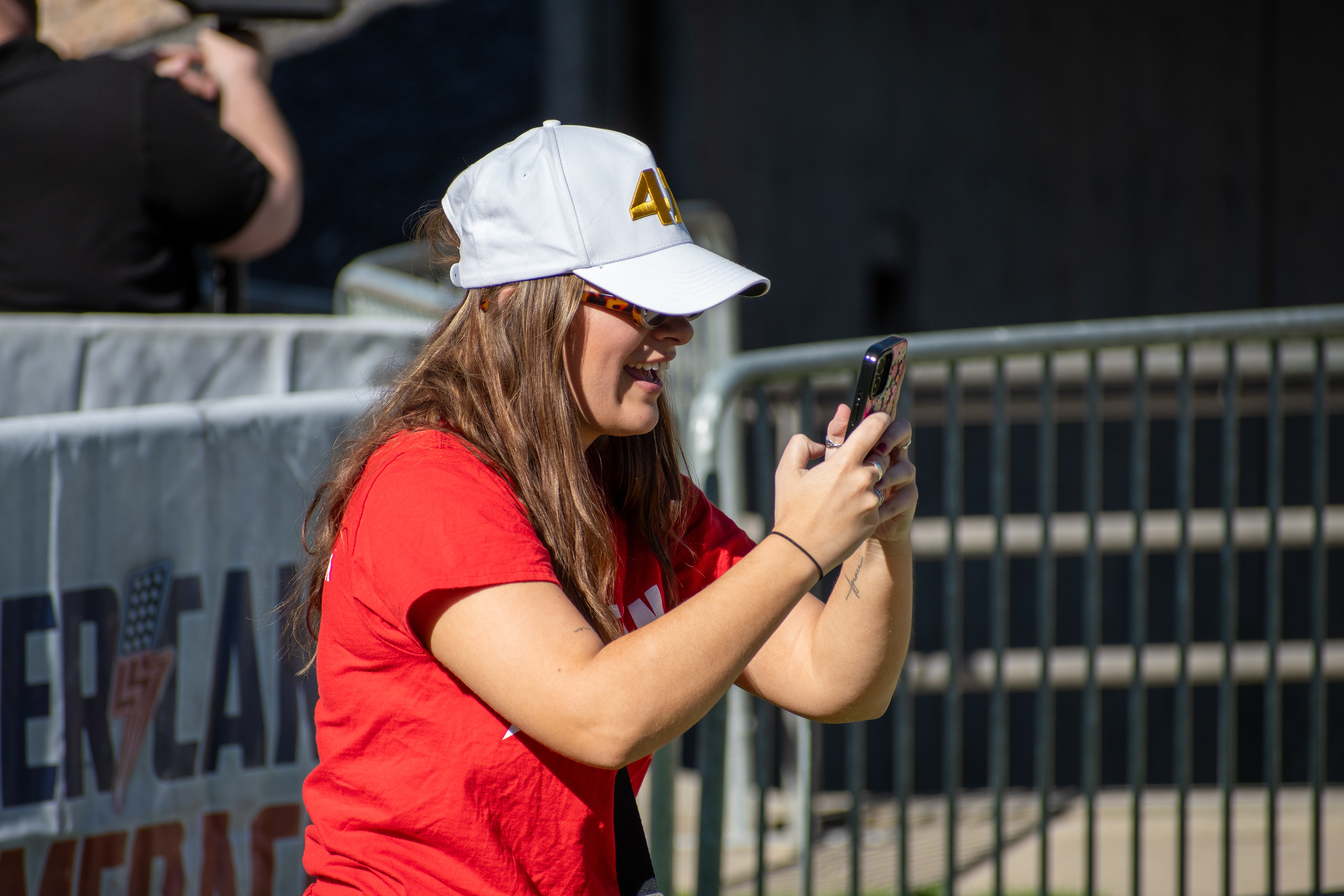 OREM, UTAH – SEPTEMBER 10, 2025: An attendee documents the scene near the barricades at Utah Valley University during the opening stop of the American Comeback Tour. Framed mid-gesture with phone in hand, the individual reflects a moment of personal engagement and quiet observation. The image captures the rhythm of participation and the emotional texture of a public gathering. © Charles-McClintock Wilson / ZUMA Press