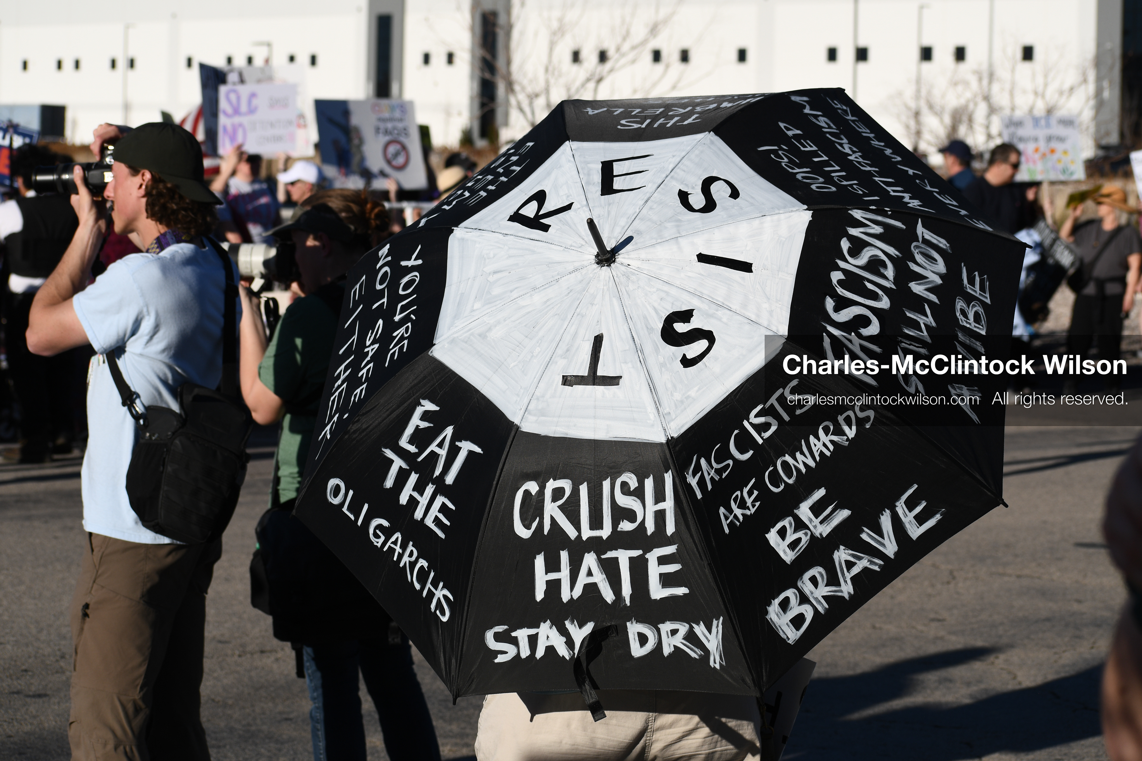 March 18, 2026, Salt Lake City, Utah, USA: A protester carries an umbrella displaying handwritten messages during a demonstration at the site of a proposed ICE detention facility on the west side of Salt Lake City. People gathered near the warehouse property as part of a community response to the planned use of the location. (Credit Image: © Charles McClintock Wilson/ZUMA Press Wire)