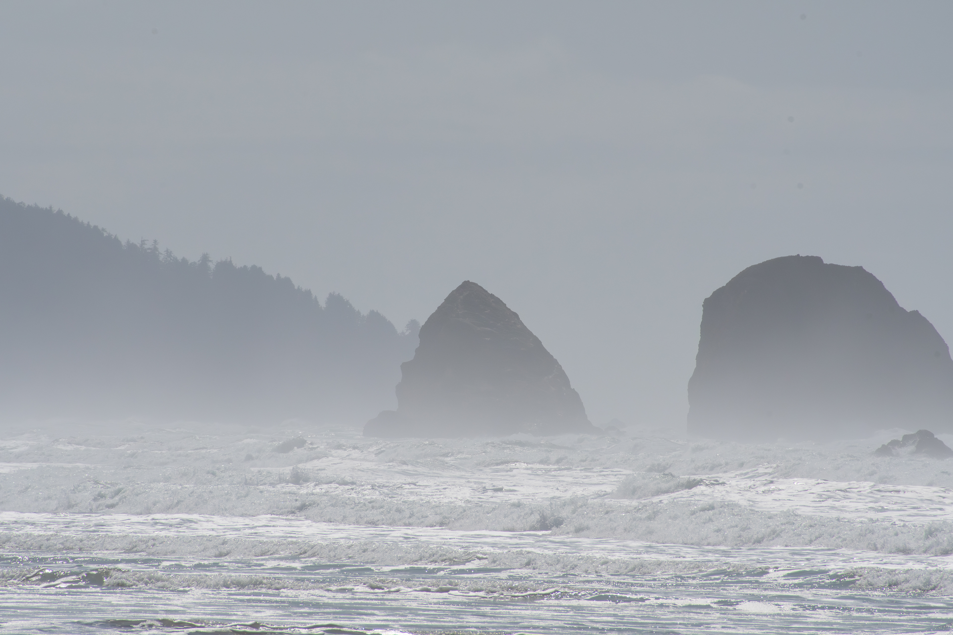 CANNON BEACH, OR, USA - APR 12, 2025: The iconic tall rock formations at Cannon Beach stand against the backdrop of a cloudy sky, creating a dramatic coastal scene along the Pacific Northwest shorelin