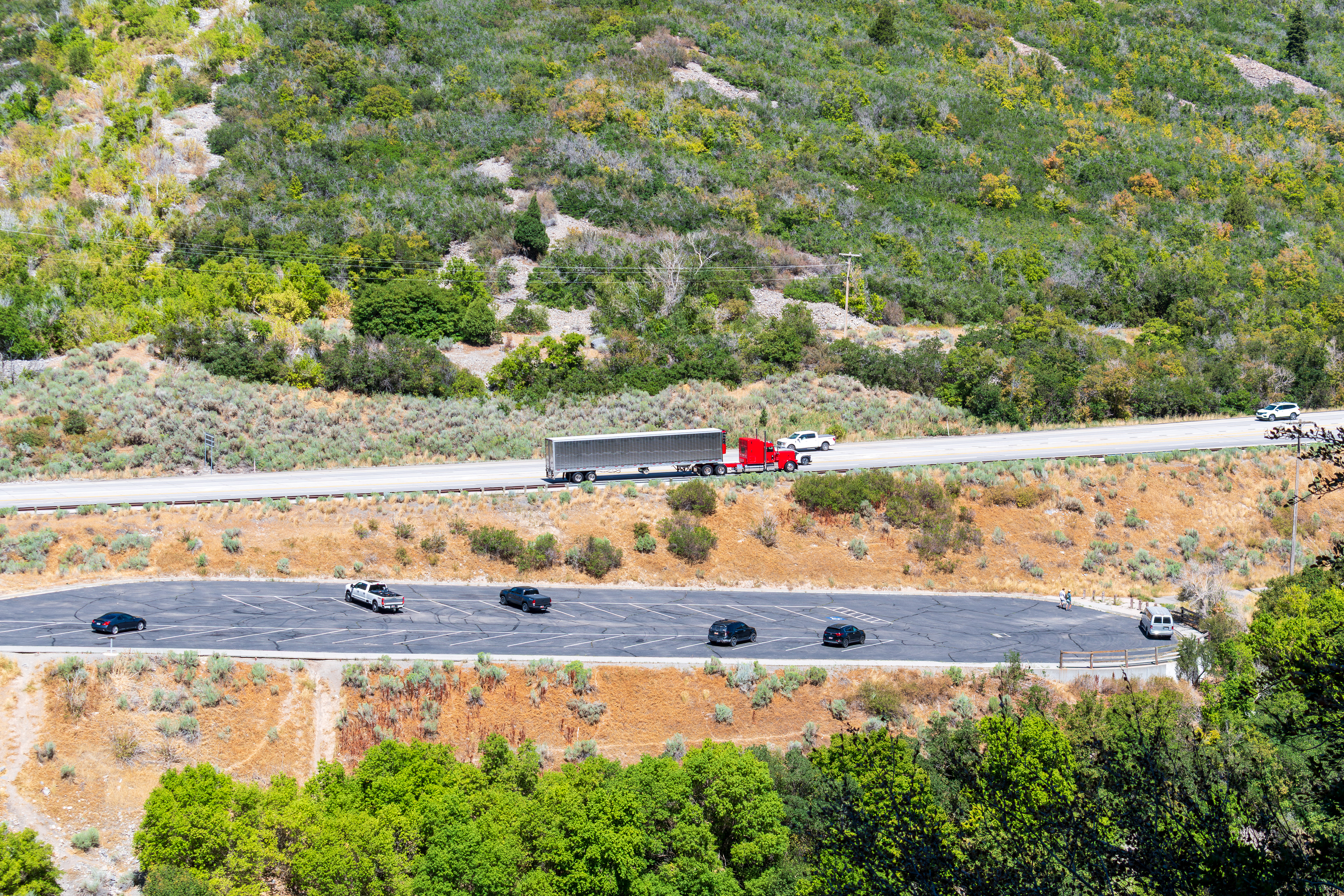 Provo, Utah, US — Sept 1, 2025: A scenic view from Bridal Veil Falls captures steep, layered rock formations and lush vegetation, with vehicles winding through the rugged terrain along U.S. Route 189.