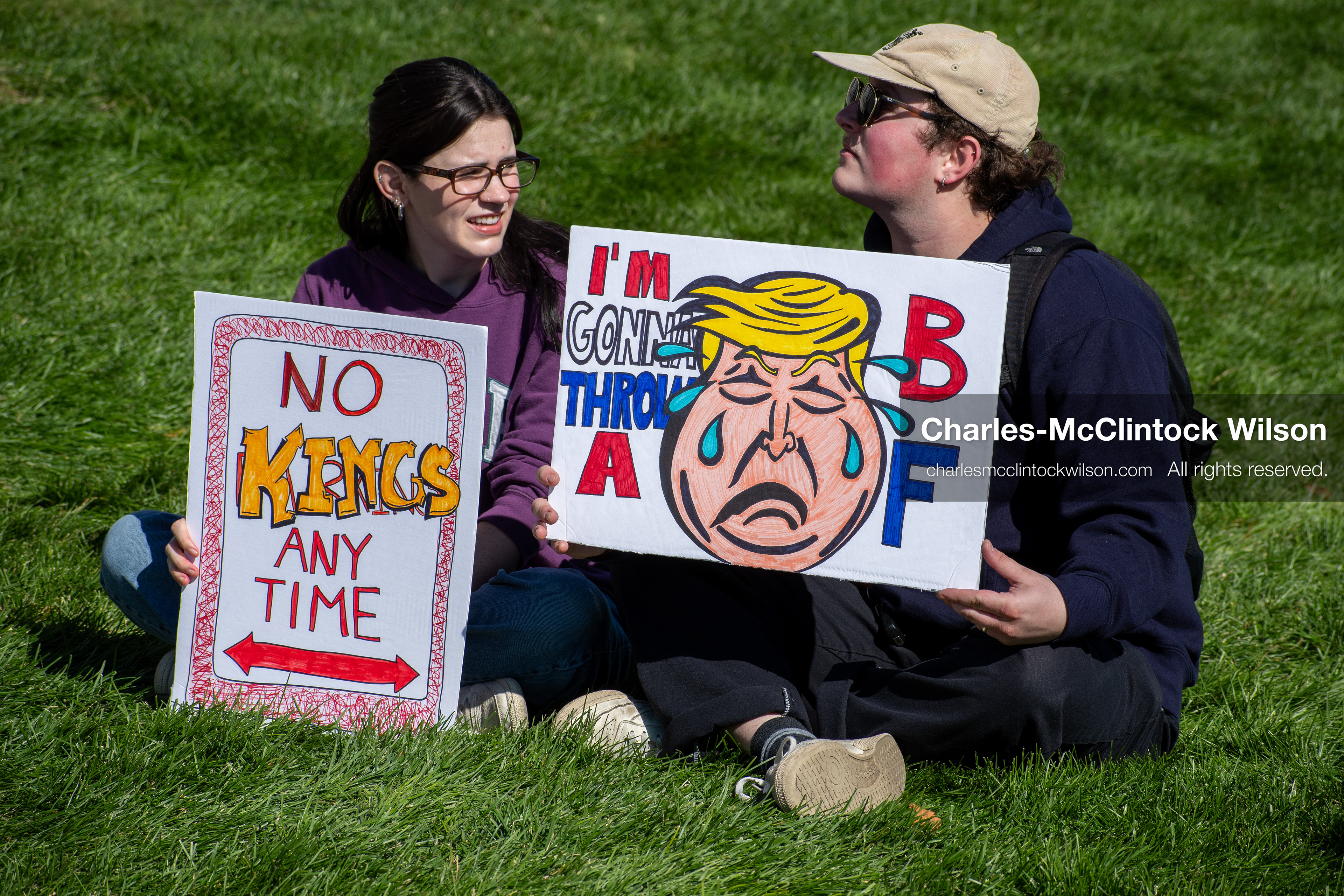 October 18, 2025, Salt Lake City, Utah, USA: Two demonstrators sit on the grass with protest signs during a "No Kings" protest at the Utah State Capitol. The protest was part of a nationwide mobilization.