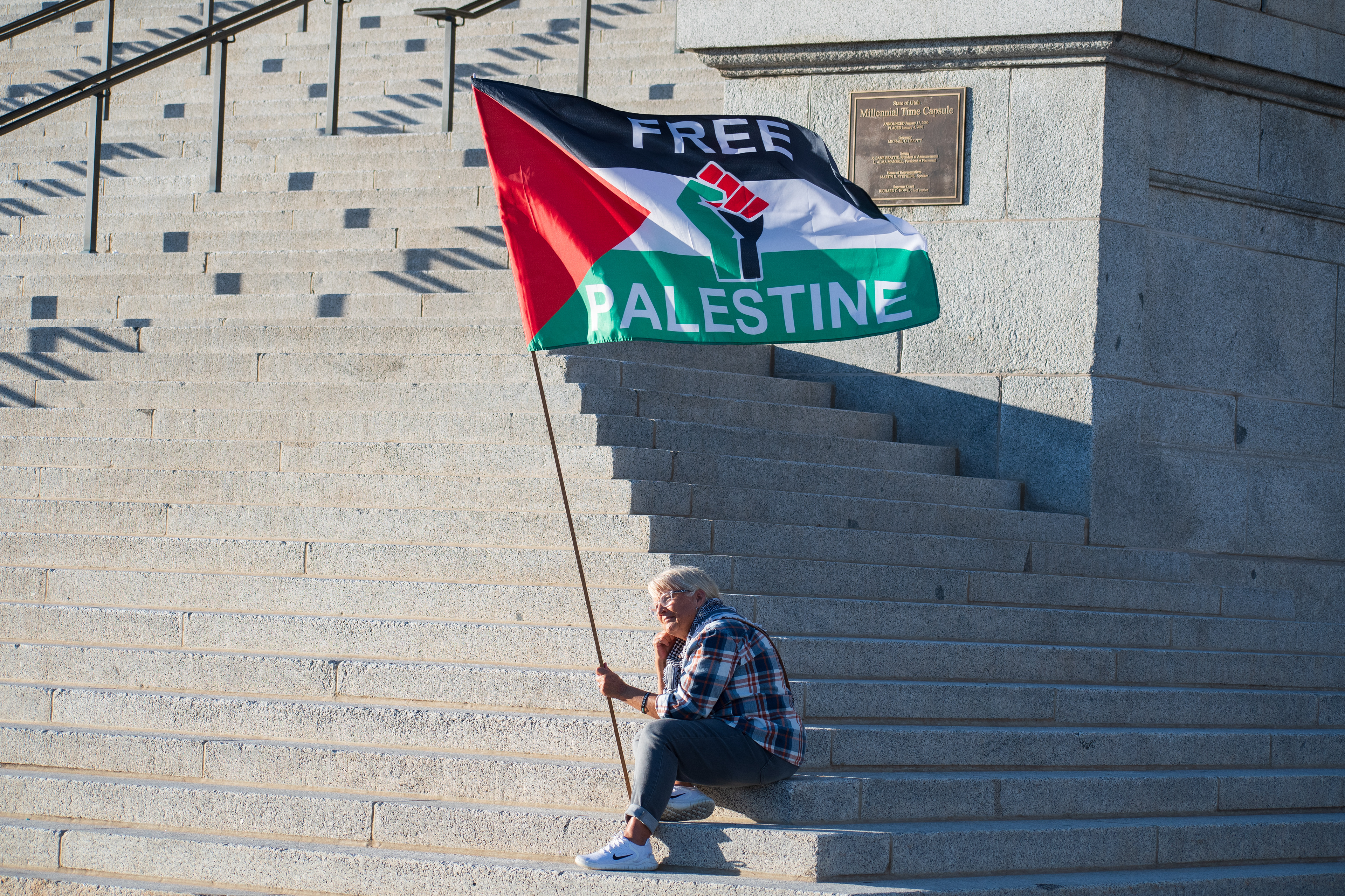October 10, 2025, Salt Lake City, Utah, USA: A demonstrator sits on the steps of the Utah State Capitol holding a flag that reads â€œFREE PALESTINEâ€ during the Free Palestine Rally. The flag features a raised fist graphic and the colors of the Palestinian flag. (Credit Image: © Charles-McClintock Wilson/ZUMA Press Wire)