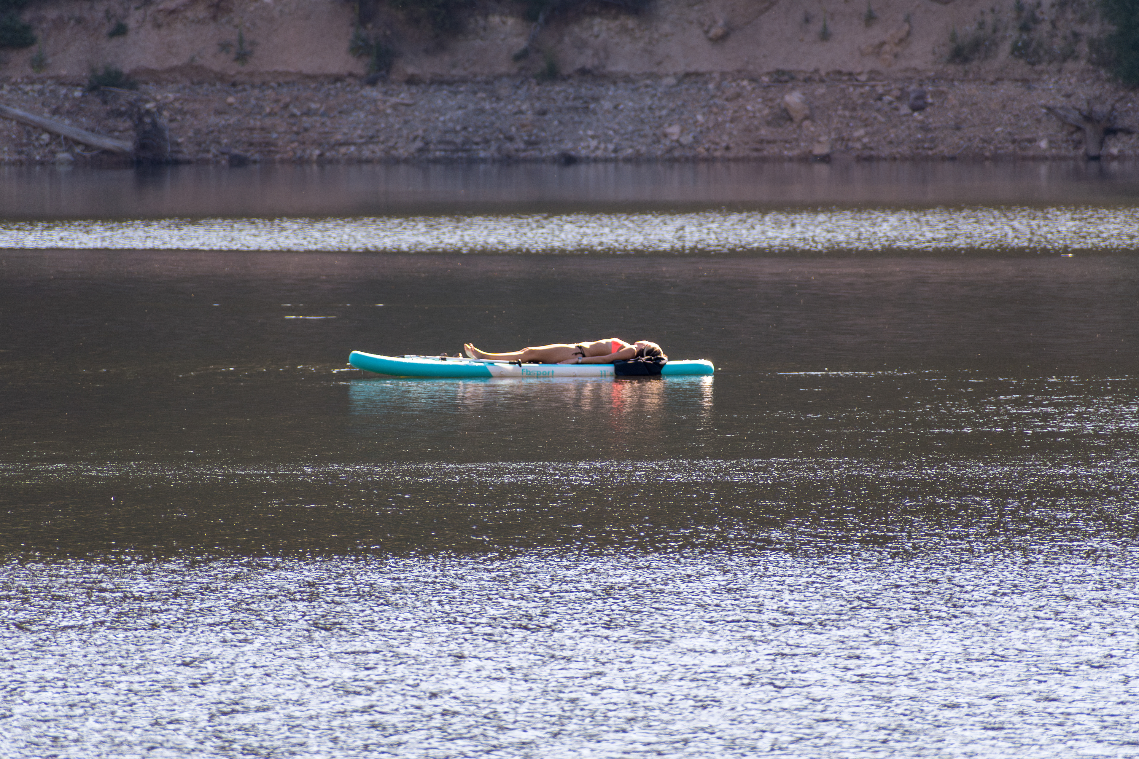 Summit County, Utah – July 20, 2025: A woman in a bikini relaxes while lying flat on a paddleboard in the calm water at Smith and Morehouse Reservoir.