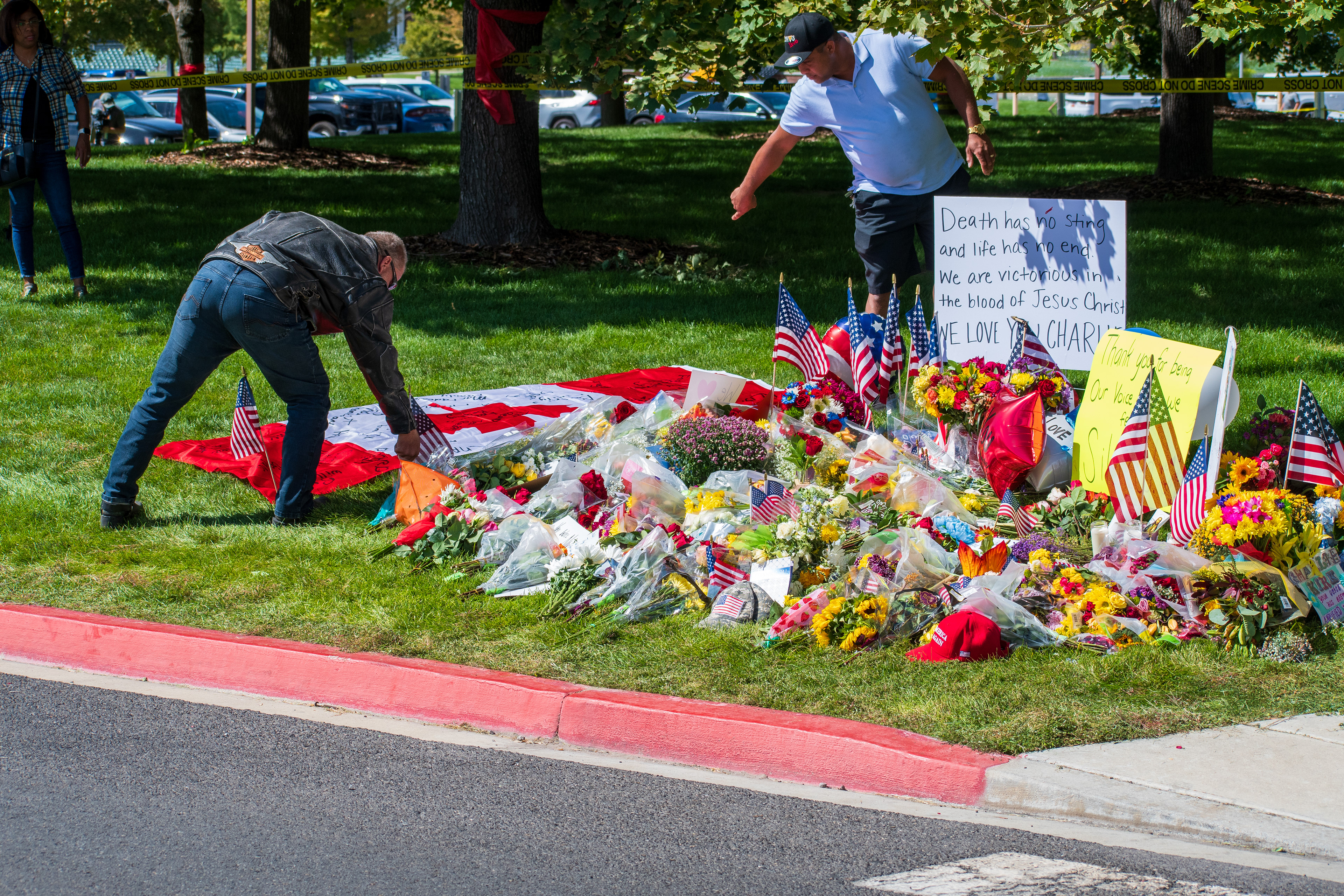 OREM, UTAH – SEPTEMBER 12, 2025: A man places small American flags beside a Canadian flag laid out on the grass at a memorial site for Charlie Kirk near Utah Valley University. Flowers and tribute items surround the display as people gather in the background. © Charles‑McClintock Wilson / ZUMA Press