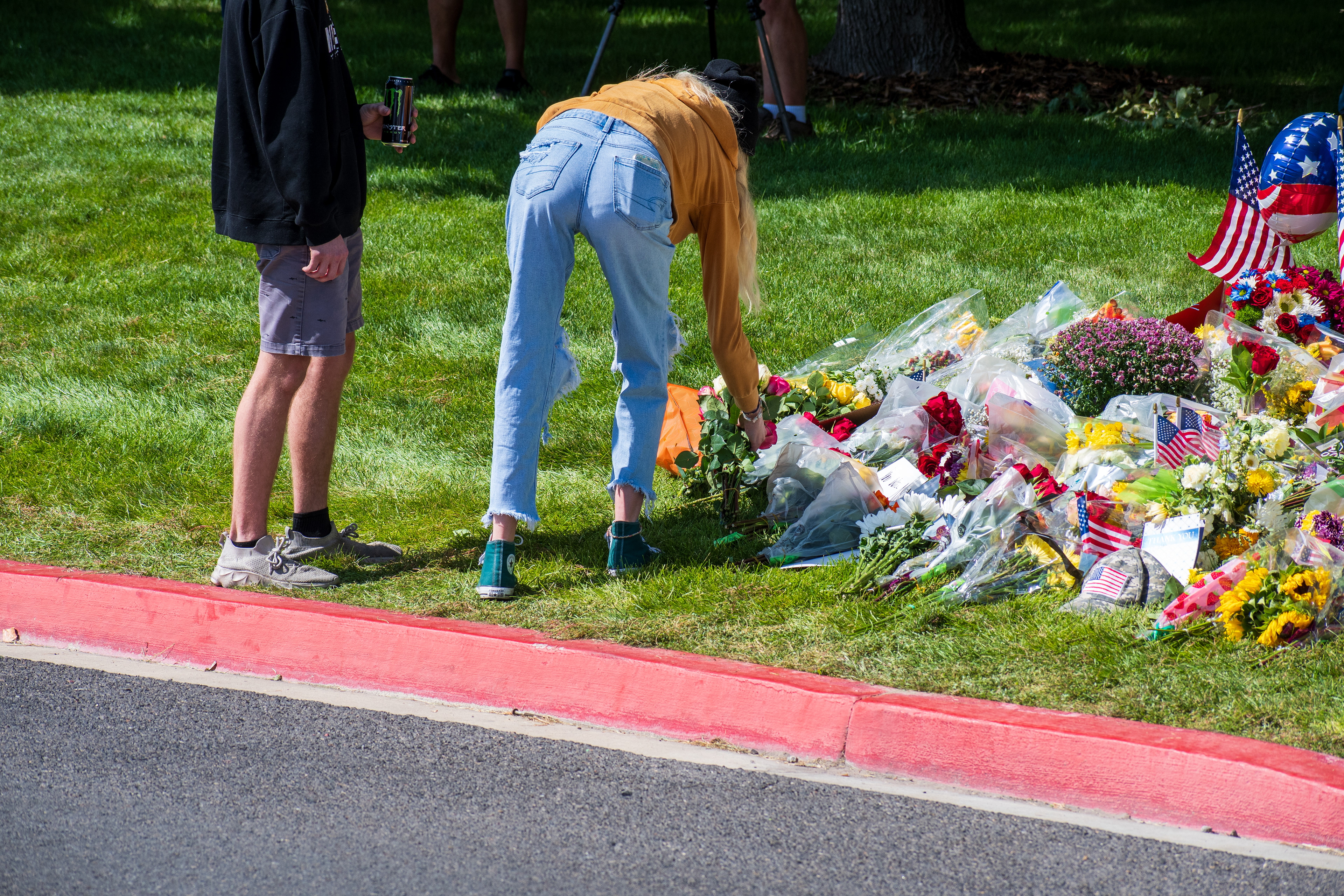 OREM, UTAH – SEPTEMBER 12, 2025: A woman kneels to arrange flowers among a growing collection of floral tributes at a memorial site for Charlie Kirk near Utah Valley University. Wrapped bouquets cover the grass as mourners gather in quiet reflection. © Charles‑McClintock Wilson / ZUMA Press
