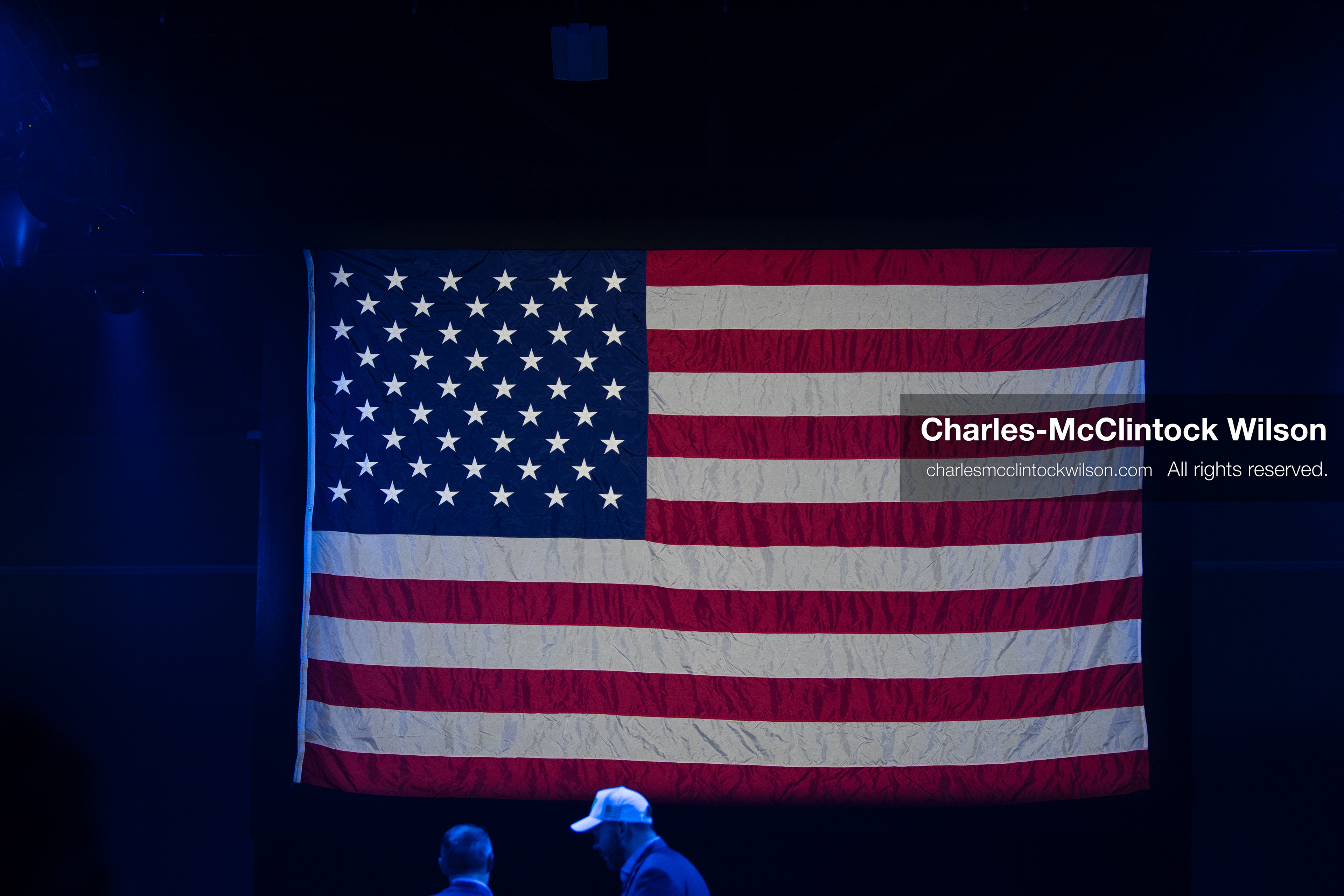 December 18, 2025, Phoenix, Arizona, USA: A large American flag hangs vertically as two attendees talk beneath its glow during AmericaFest 2025 at the Phoenix Convention Center, the first edition of the event held since the death of Charlie Kirk. (Credit Image: (c) Charles-McClintock Wilson/ZUMA Press Wire)