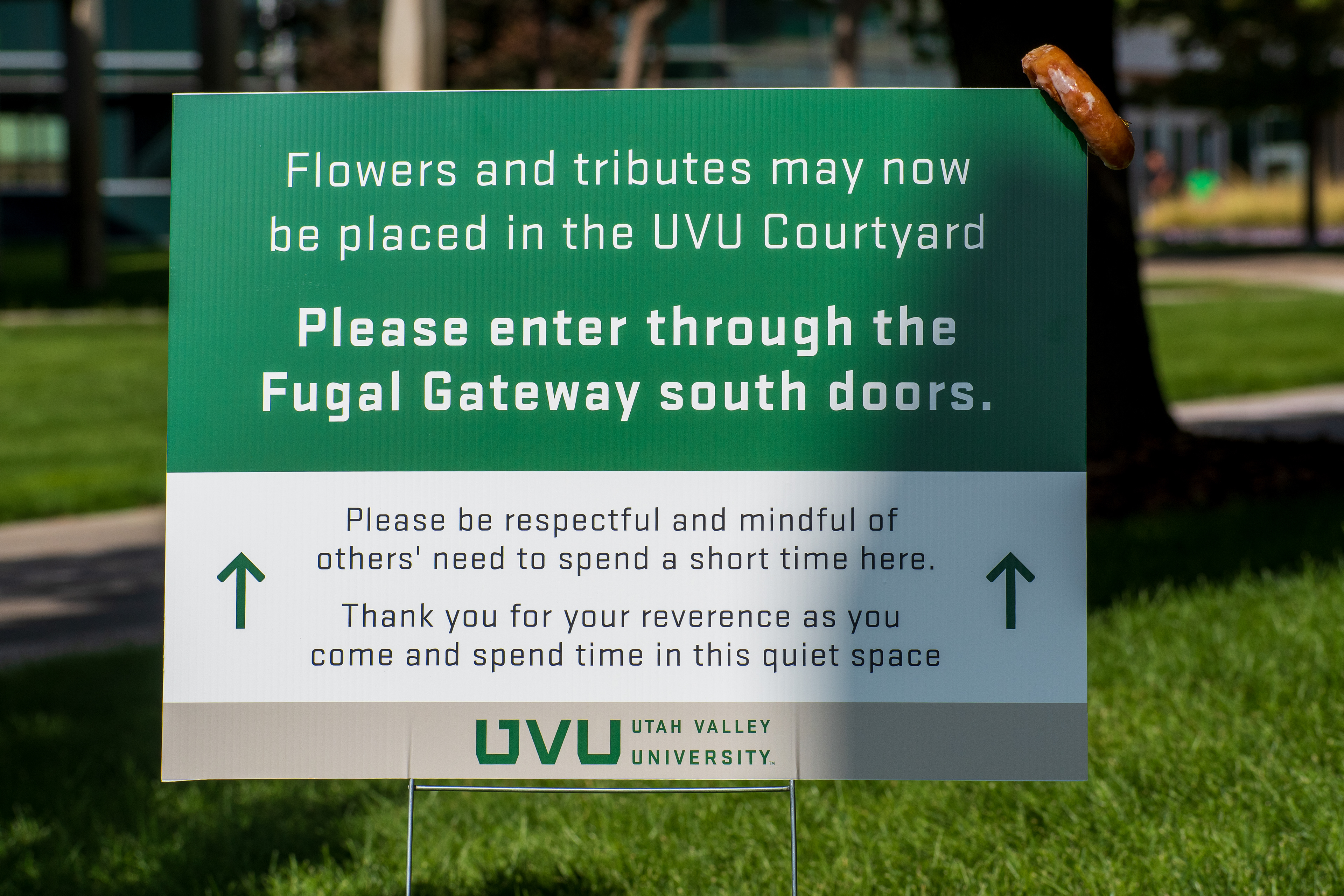 OREM, UTAH – SEPTEMBER 15, 2025: A sign posted on the campus of Utah Valley University provides instructions for placing flowers and tributes in the UVU Courtyard. The message asks visitors to enter through the Fugal Gateway south doors and to be respectful of others. A small object, possibly a bagel or donut, hangs from the top corner of the sign. © Charles‑McClintock Wilson / ZUMA Press