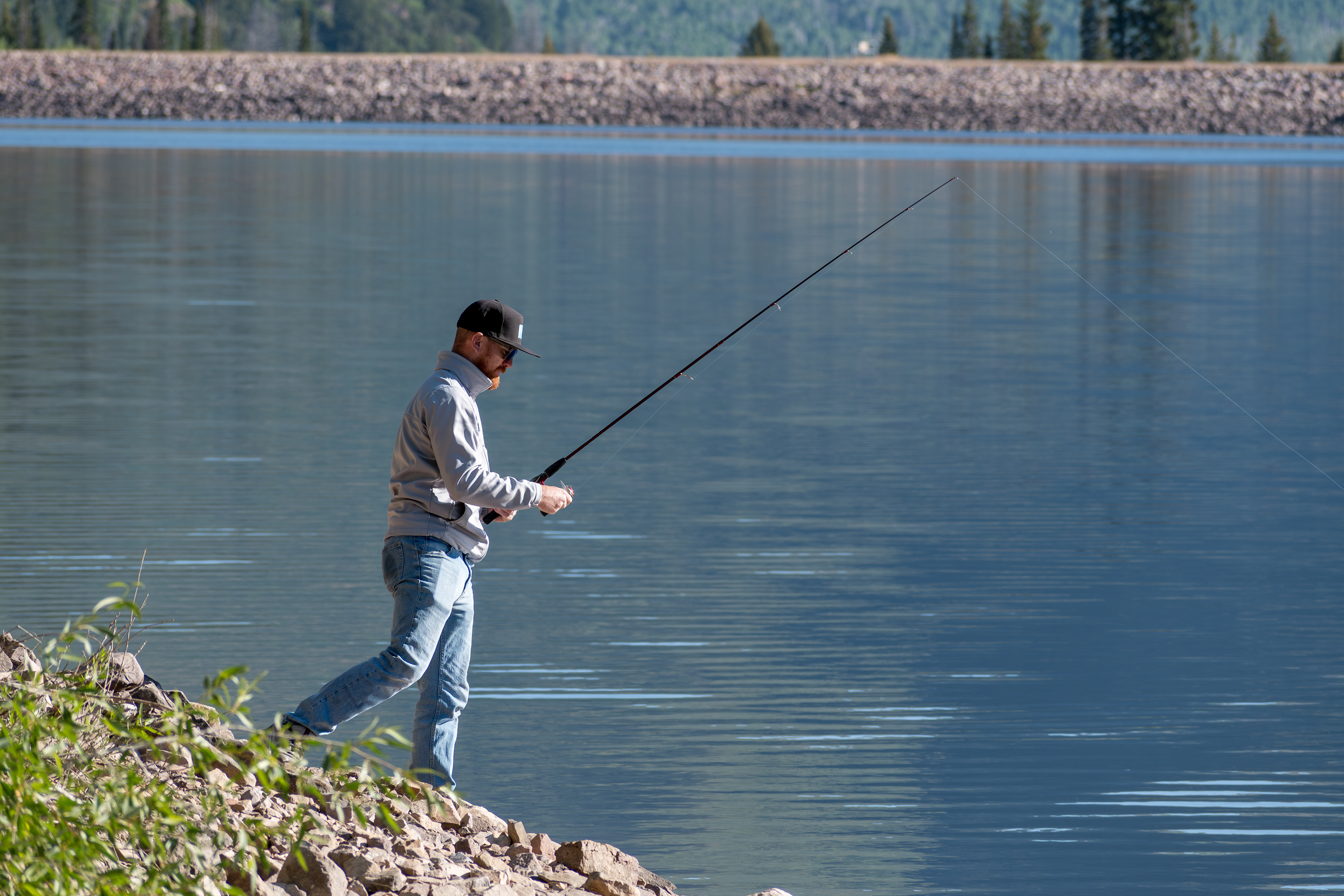 Summit County, Utah – July 20, 2025: A man fishes alone on the calm waters of Smith and Morehouse Reservoir during a quiet summer day.