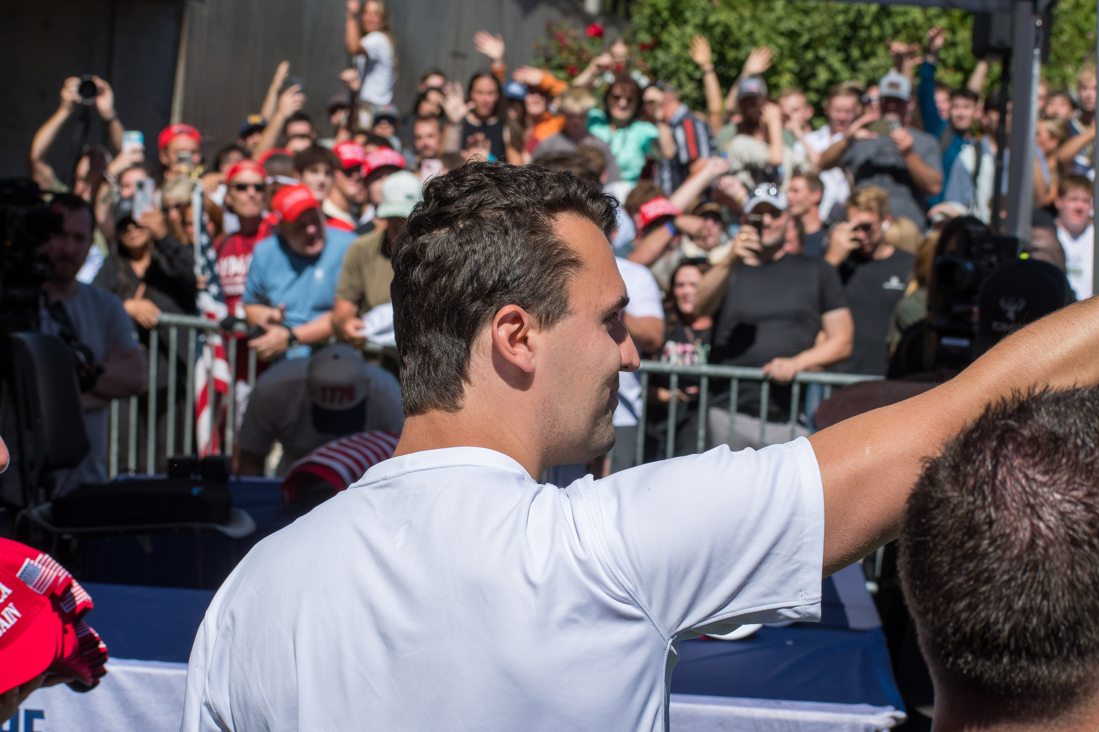 Charlie Kirk stands before a crowd of supporters during a public event at Utah Valley University. Separated by metal barricades, attendees raise phones and cheer as Kirk addresses them in one of his final public moments. The image reflects the intensity of civic engagement and the charged atmosphere that defined the gathering. © Charles-McClintock Wilson / ZUMA Press