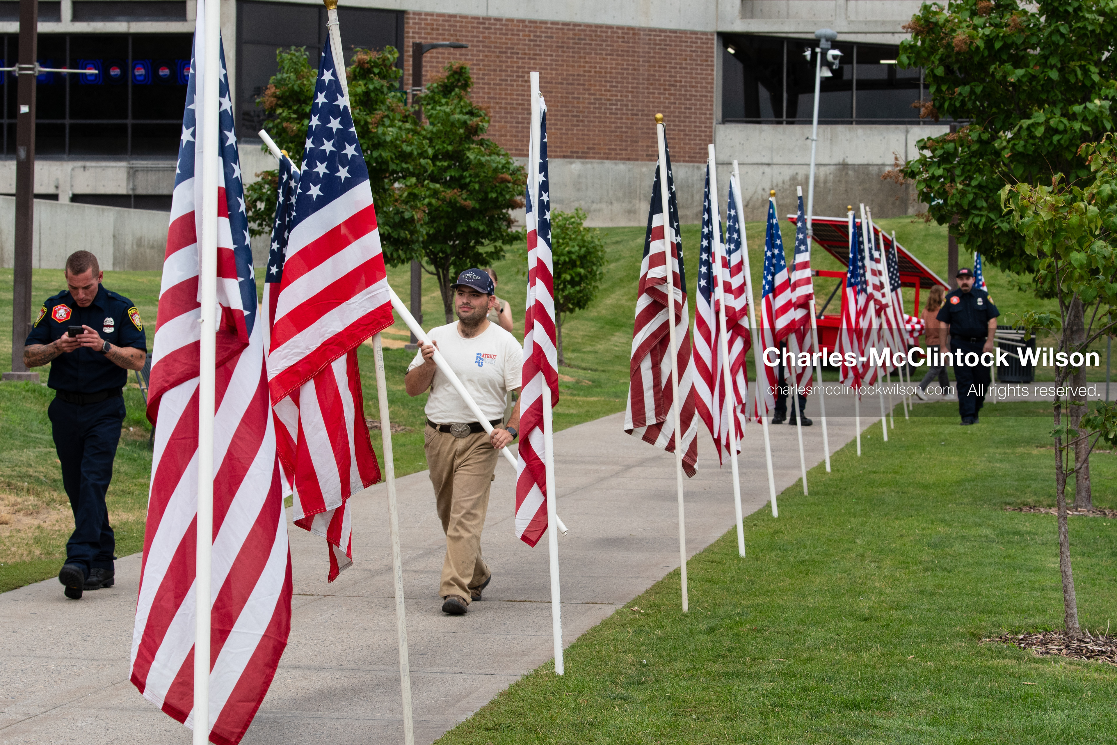 Volunteers and first responders carry American flags along a concrete walkway outside the UCCU Center at Utah Valley University in Orem, Utah, on Wednesday, July 29, 2026. The temporary memorial display was set up to line the path for attendees arriving at the public memorial ceremony honoring Provo Fire Captain Spencer Long and his family. (Photo by Charles-McClintock Wilson/Sipa USA)