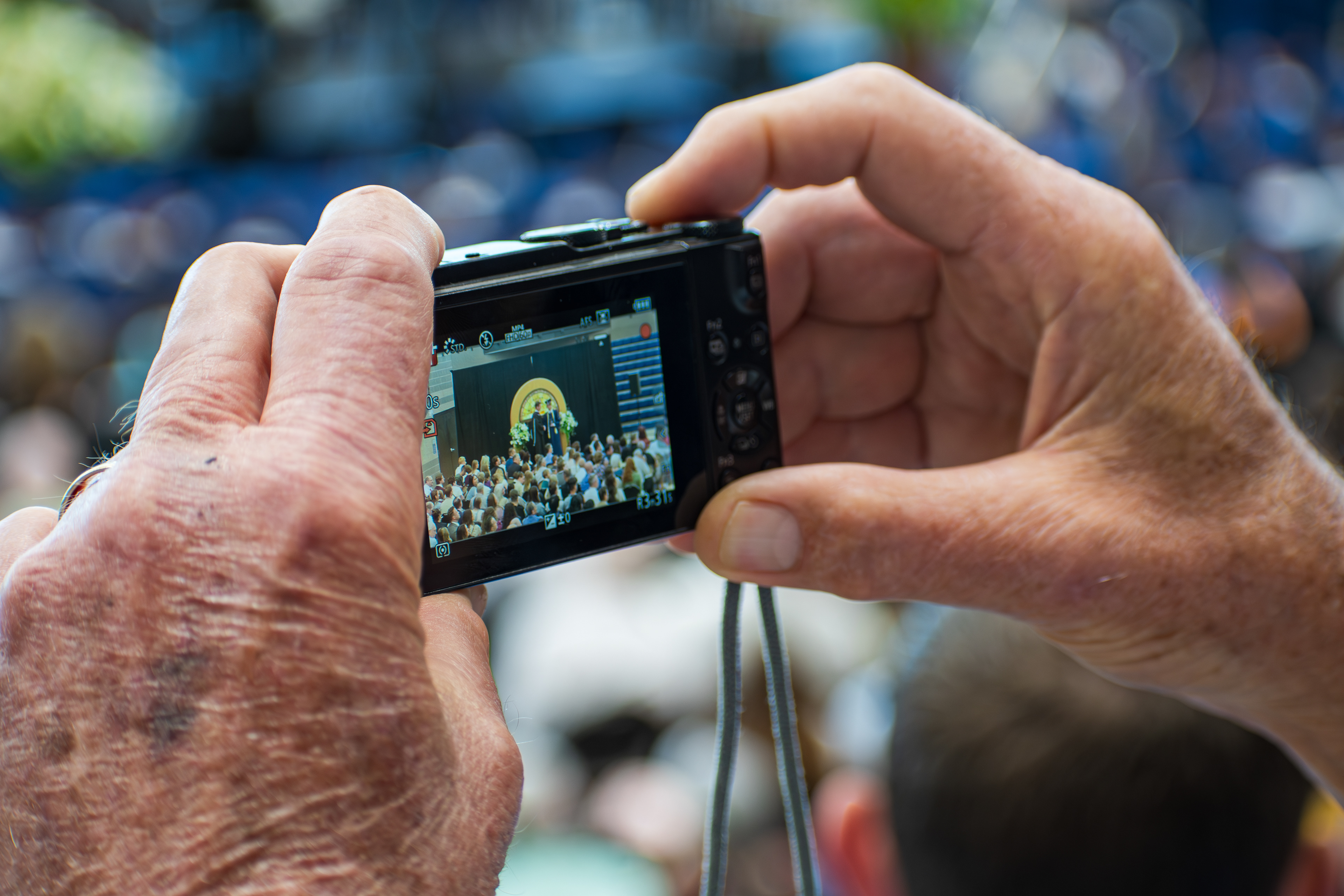 American Fork, UT, USA – May 24, 2025: An elderly individual records a graduation ceremony at an academy in American Fork, Utah, using a digital camera.