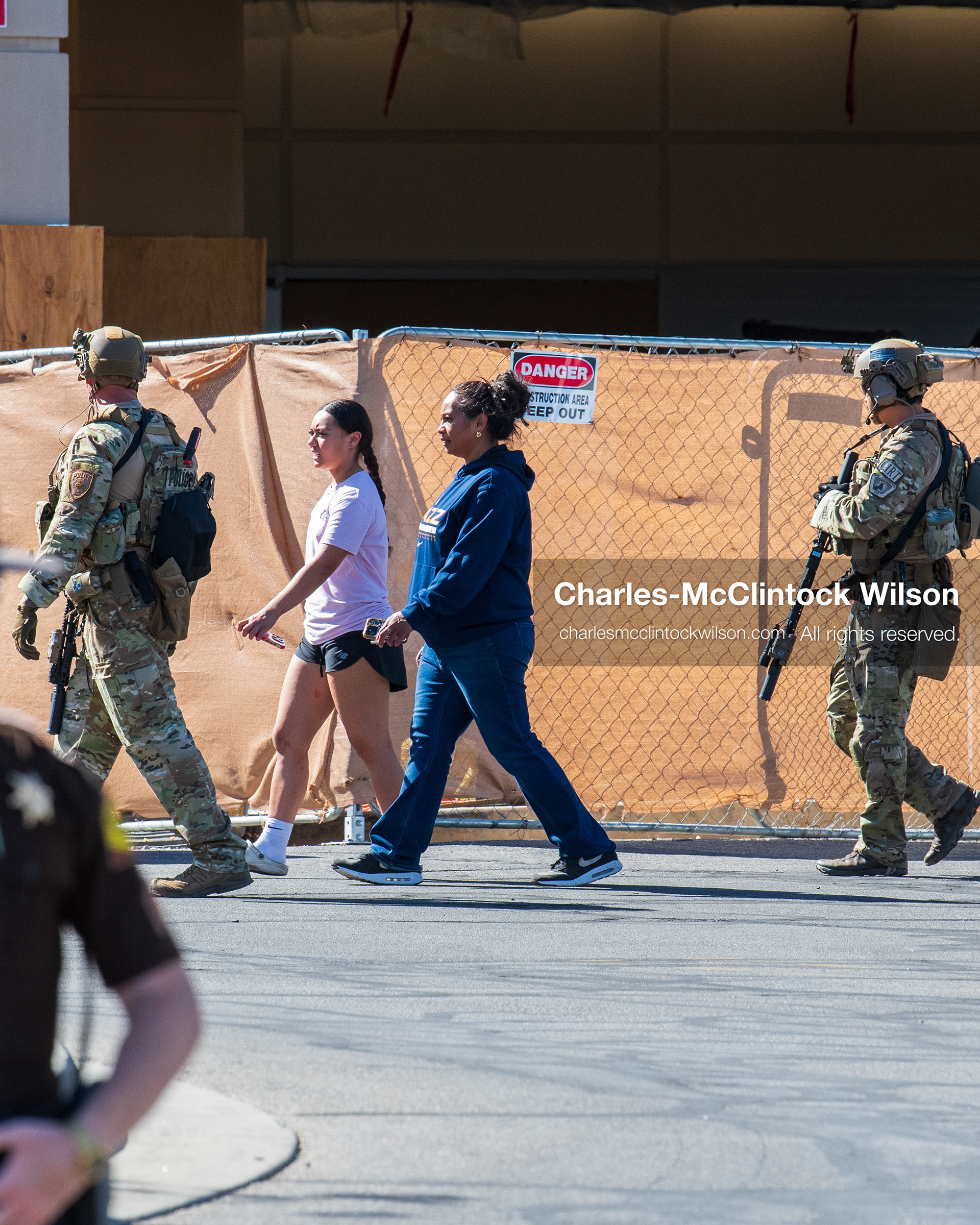Armed law enforcement officers in tactical gear escort two civilians past a construction barrier outside Intermountain Medical Center in Murray, Utah, on Monday, August 17, 2026. Multiple regional law enforcement agencies converged to heavily secure the hospital perimeter as a safety precaution after shooting victims arrived from a fatal shootout that erupted outside a funeral service in nearby Kearns earlier that day. (Photo by Charles-McClintock Wilson/Sipa USA)