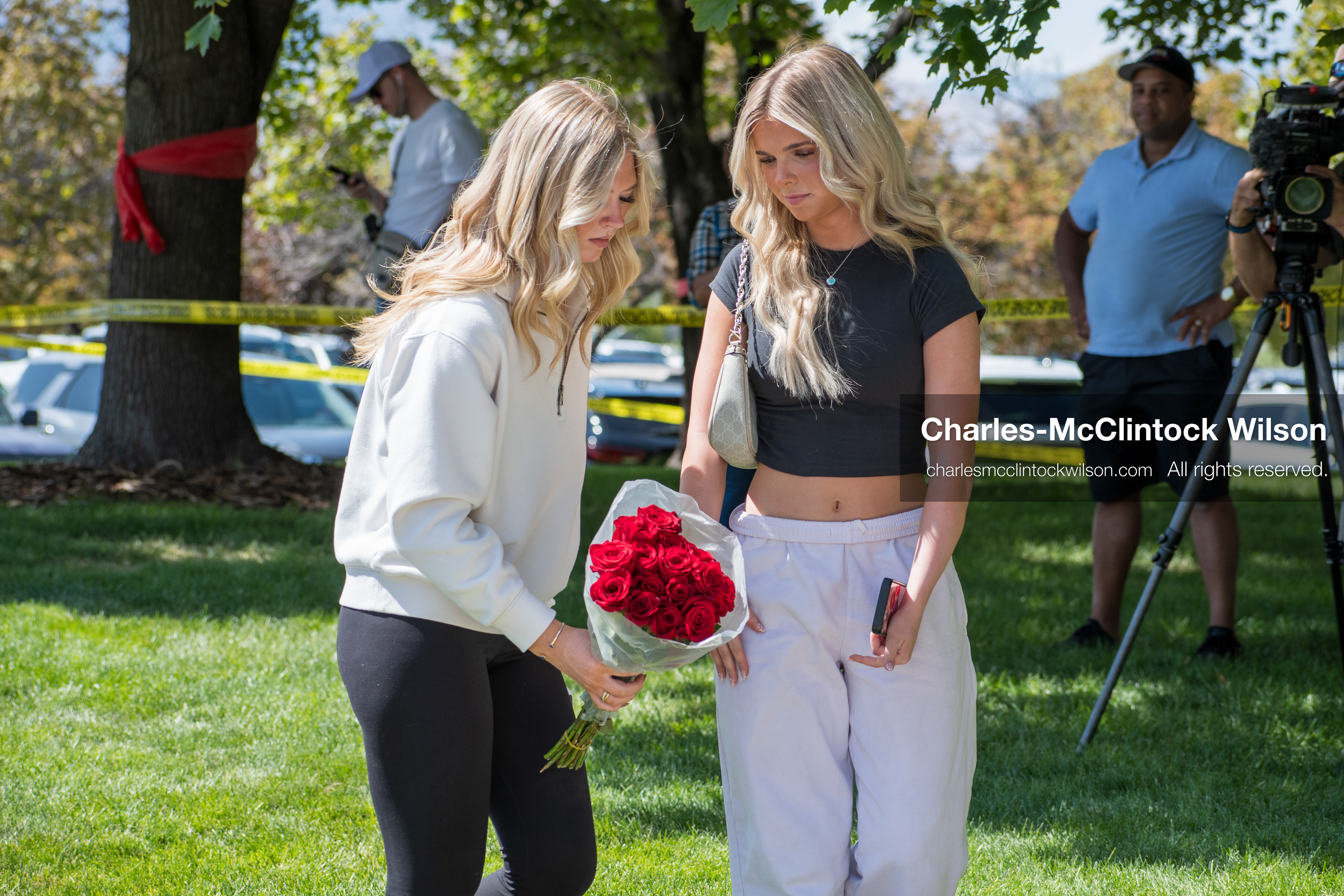 OREM, UTAH – SEPTEMBER 12, 2025: Two individuals stand at a memorial site for Charlie Kirk near Utah Valley University, one holding a bouquet of red roses. In the background, others gather and document the scene as part of a tribute event. © Charles‑McClintock Wilson / ZUMA Press