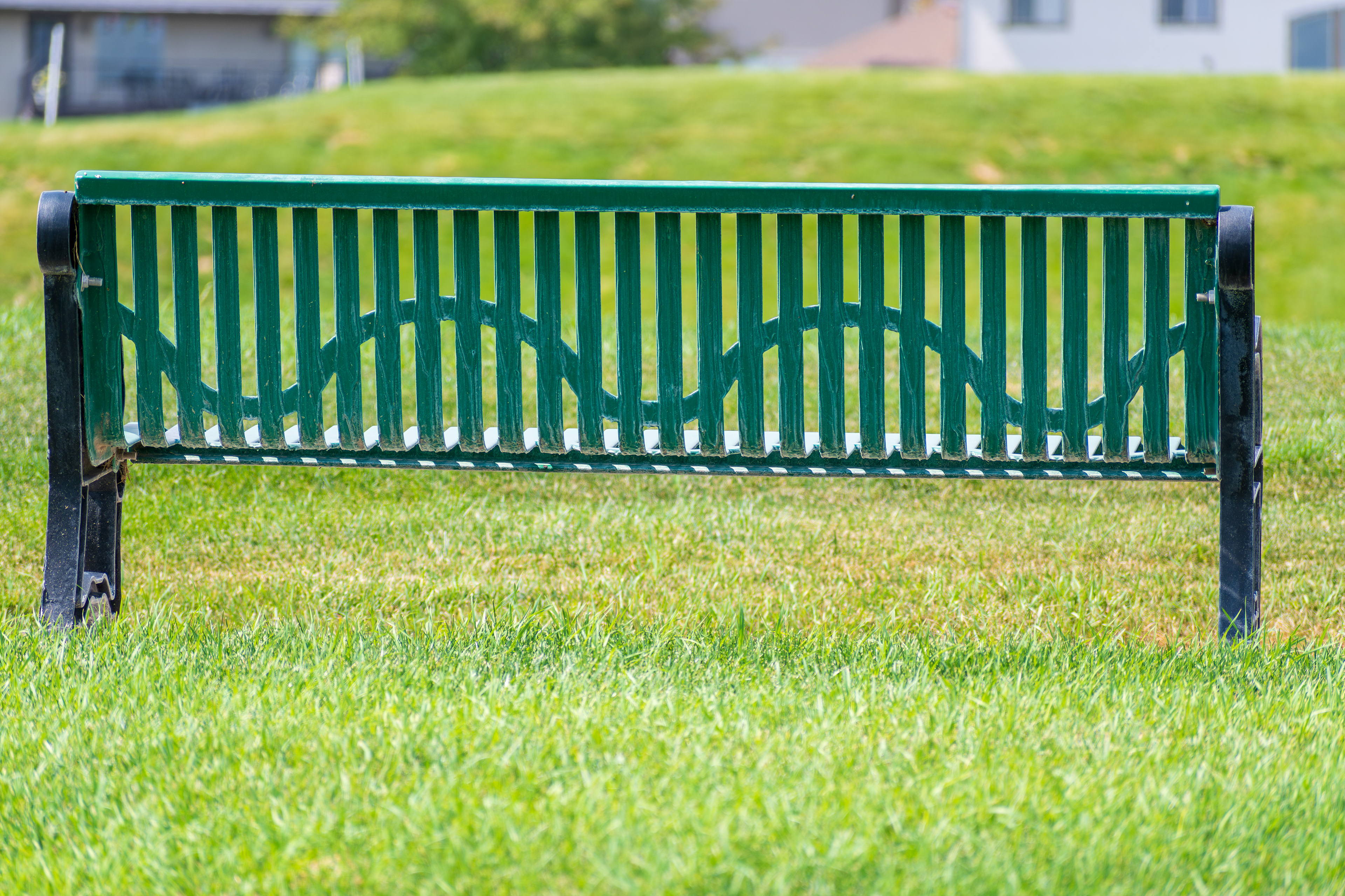 Salt Lake City, Utah, USA — September 1, 2025: A green metal park bench sits on a grassy area near a sidewalk with mountain terrain in the background.