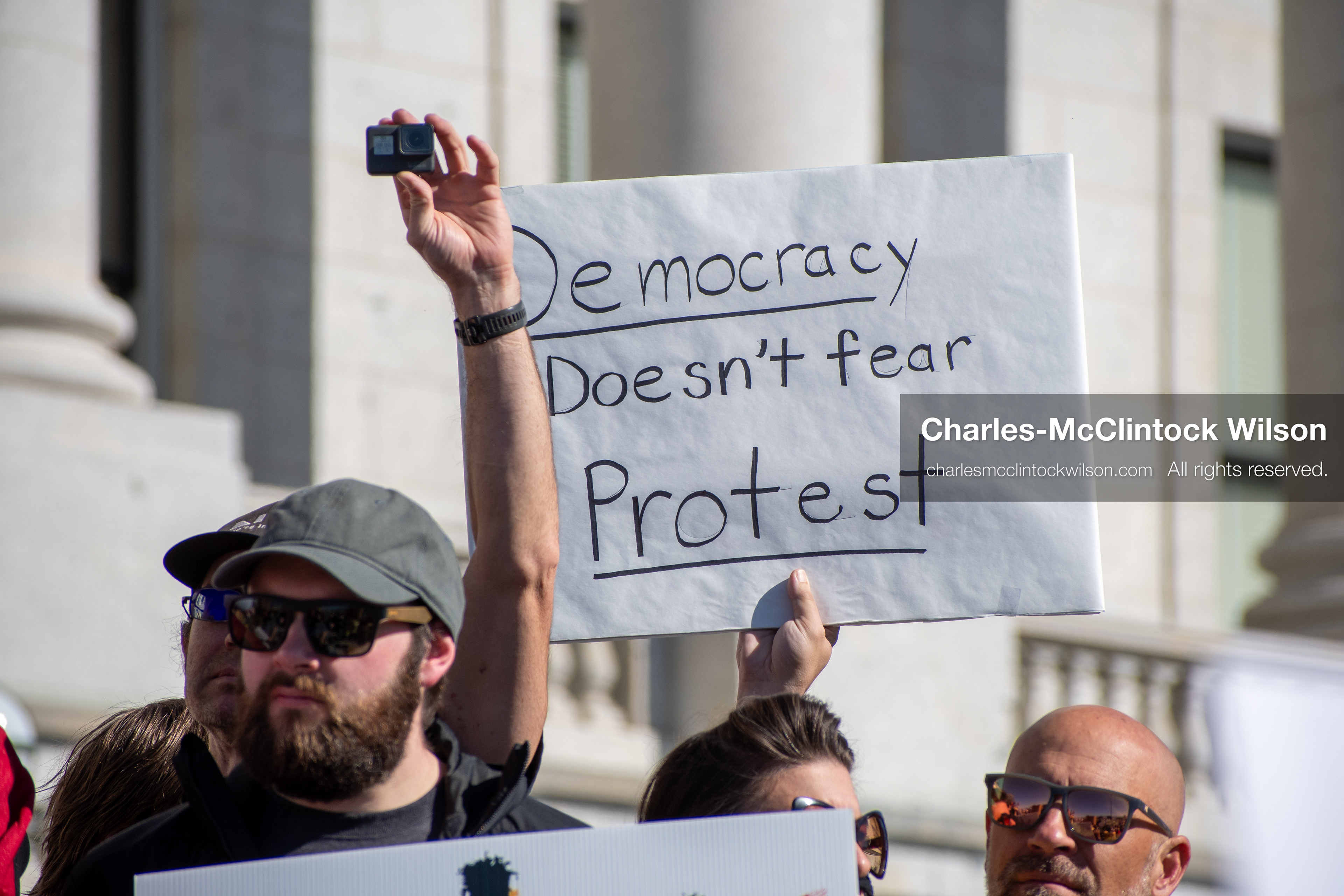 October 18, 2025, Salt Lake City, Utah, USA: A demonstrator raises a placard during a "No Kings" protest held at the Utah State Capitol. Other participants and signs are visible in the background during the public gathering.