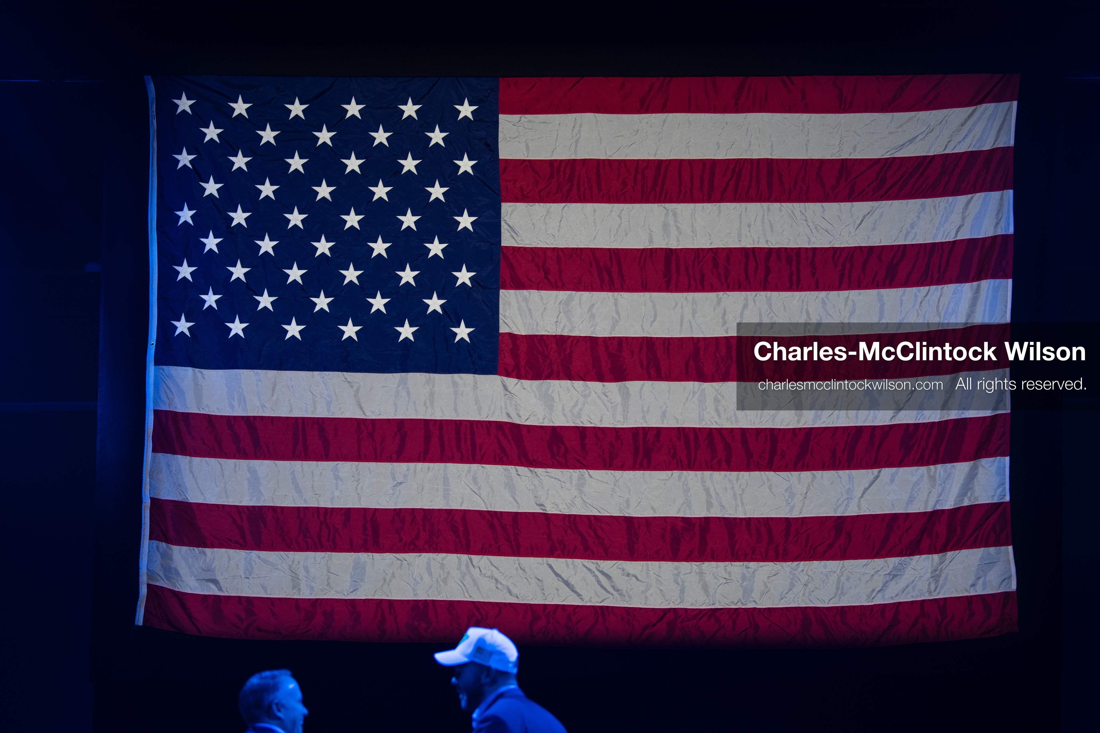 December 18, 2025, Phoenix, Arizona, USA: A large American flag hangs vertically as two attendees talk beneath its glow during AmericaFest 2025 at the Phoenix Convention Center, the first edition of the event held since the death of Charlie Kirk. (Credit Image: (c) Charles-McClintock Wilson/ZUMA Press Wire)