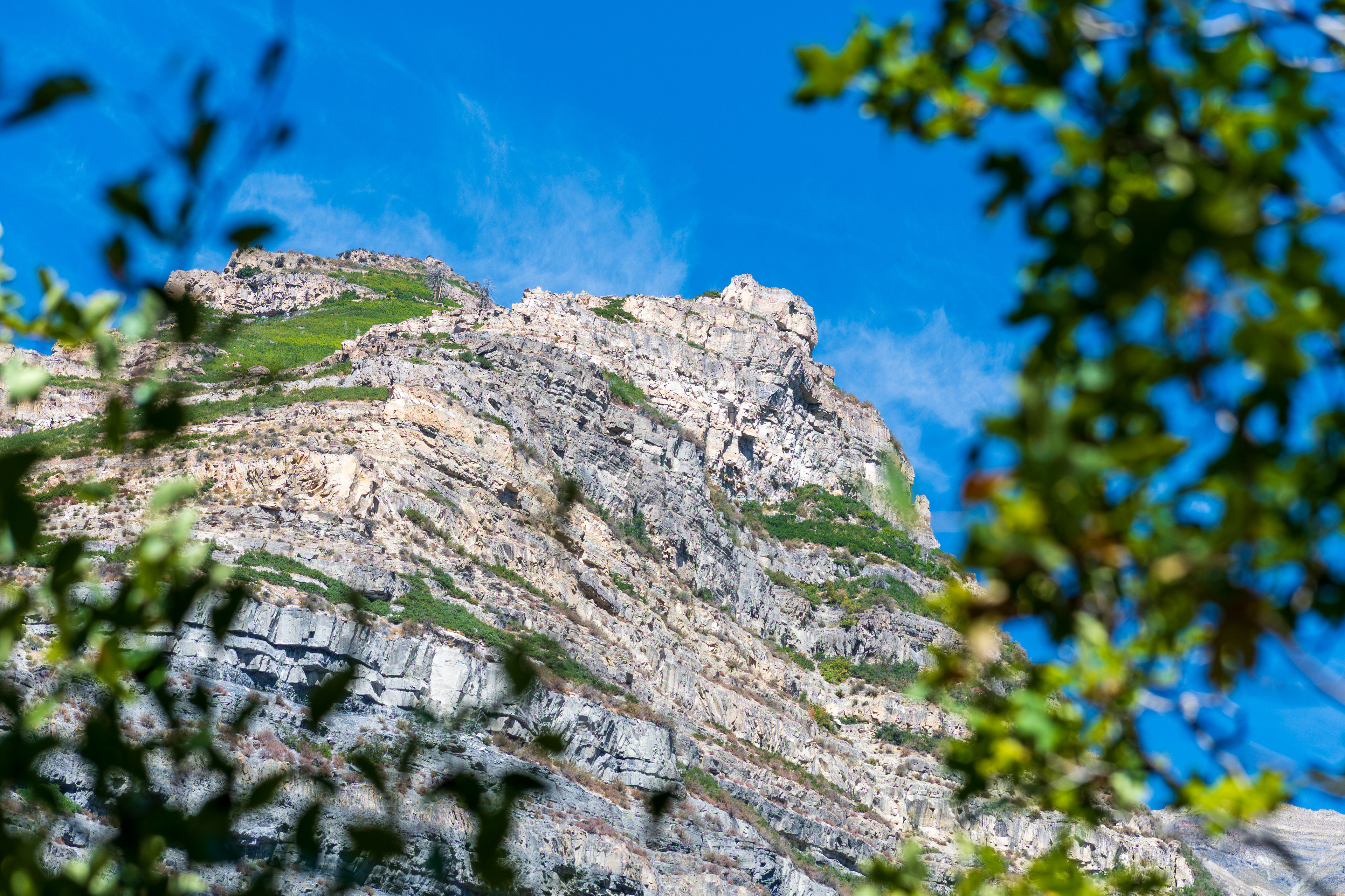 Provo, Utah, USA — September 1, 2025: Rugged mountain slopes rise under a clear blue sky, with layered rock formations and sparse vegetation defining the terrain near Bridal Veil Falls in Provo, Utah.