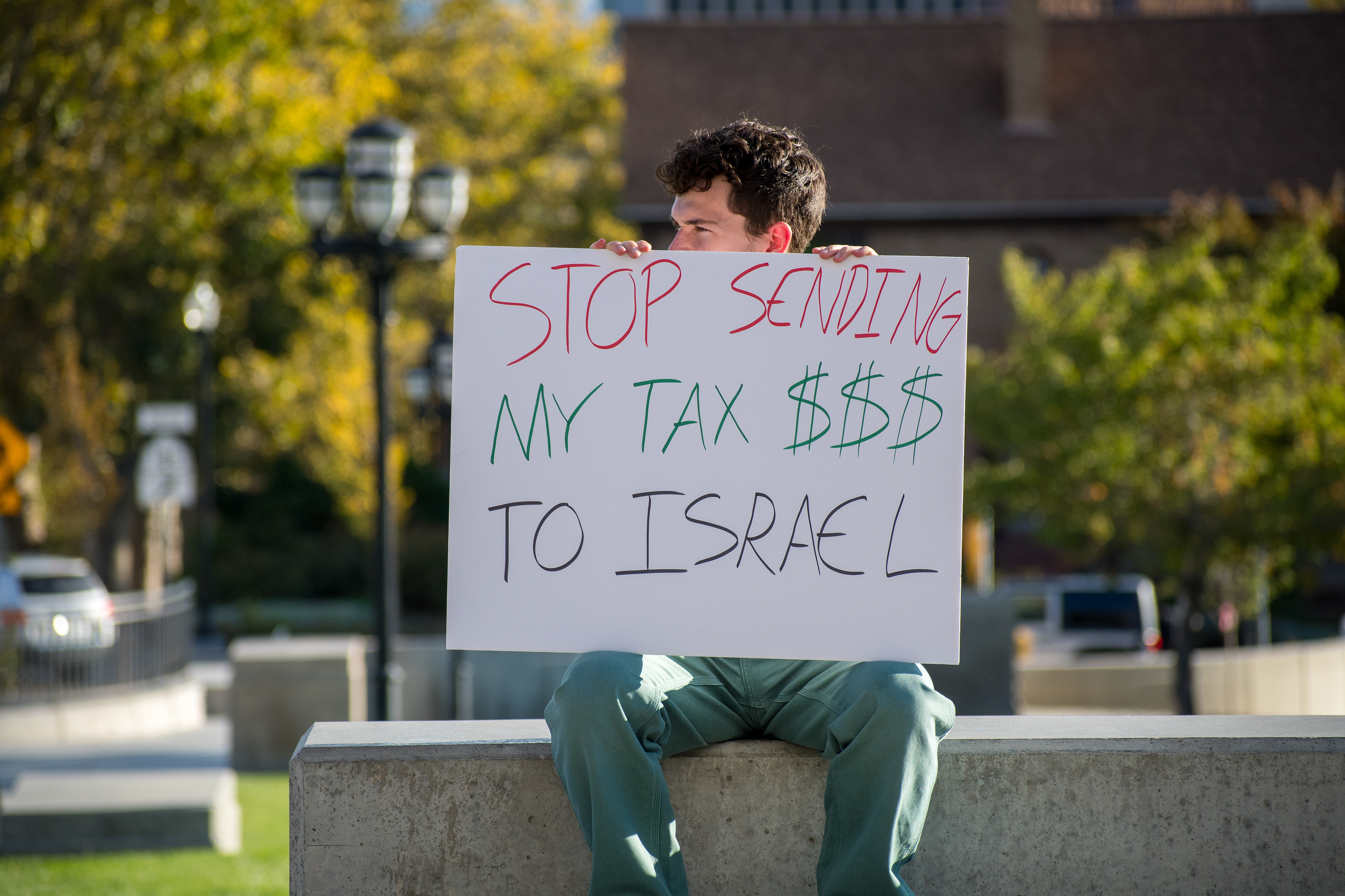 October 10, 2025, Salt Lake City, Utah, USA: A demonstrator sits on a concrete ledge during the Free Palestine Rally organized in front of the Utah State Capitol. Trees and civic buildings frame the background as participants gather in protest. (Credit Image: © Charles-McClintock Wilson/ZUMA Press Wire)