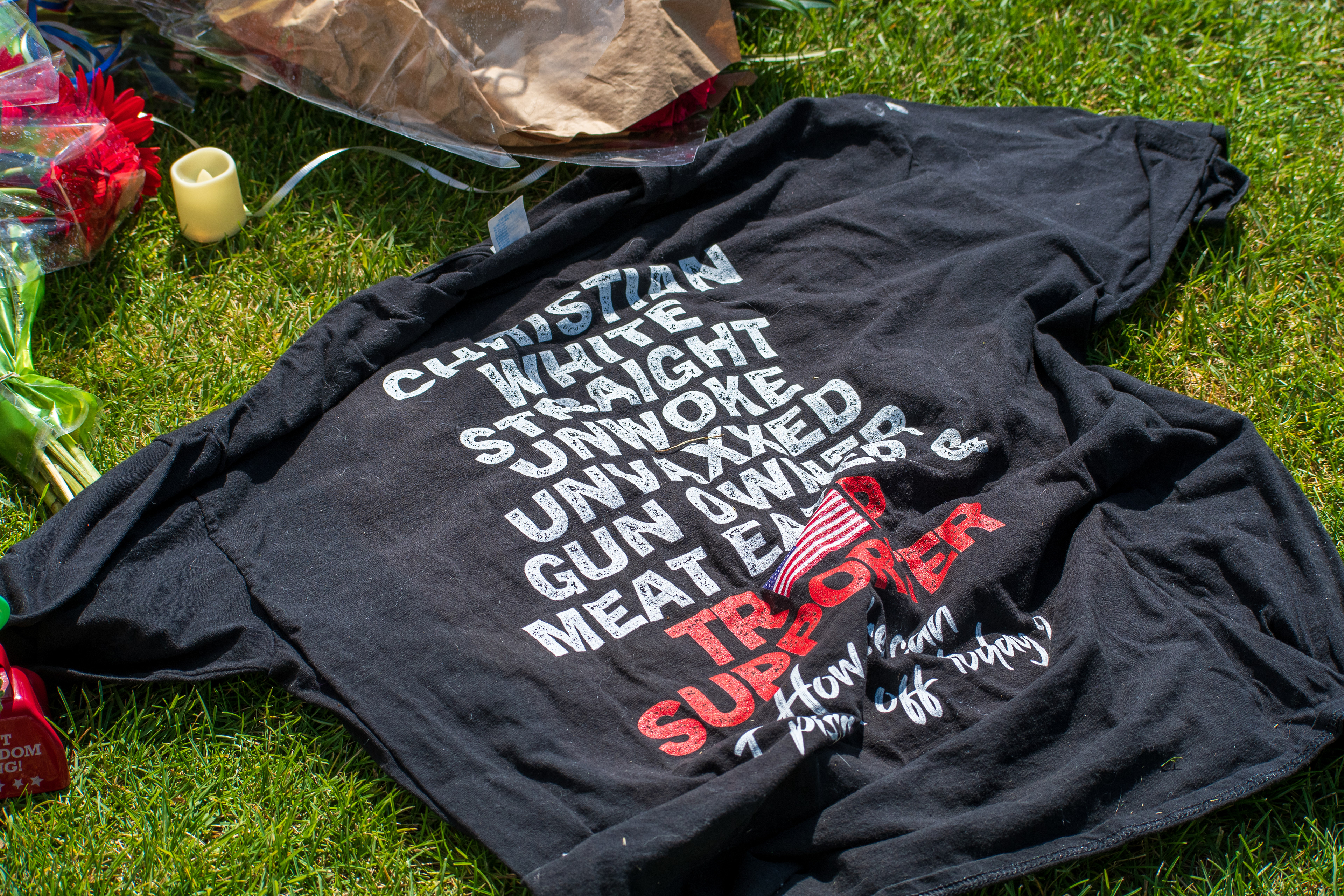 OREM, UTAH – SEPTEMBER 12, 2025: A black t-shirt bearing bold ideological statements is displayed at a memorial site for Charlie Kirk outside Timpanogos Regional Hospital. Surrounded by flowers, a candle, and a brown paper bag, the shirt includes printed text referencing religious, political, and cultural identity. © Charles‑McClintock Wilson / ZUMA Press