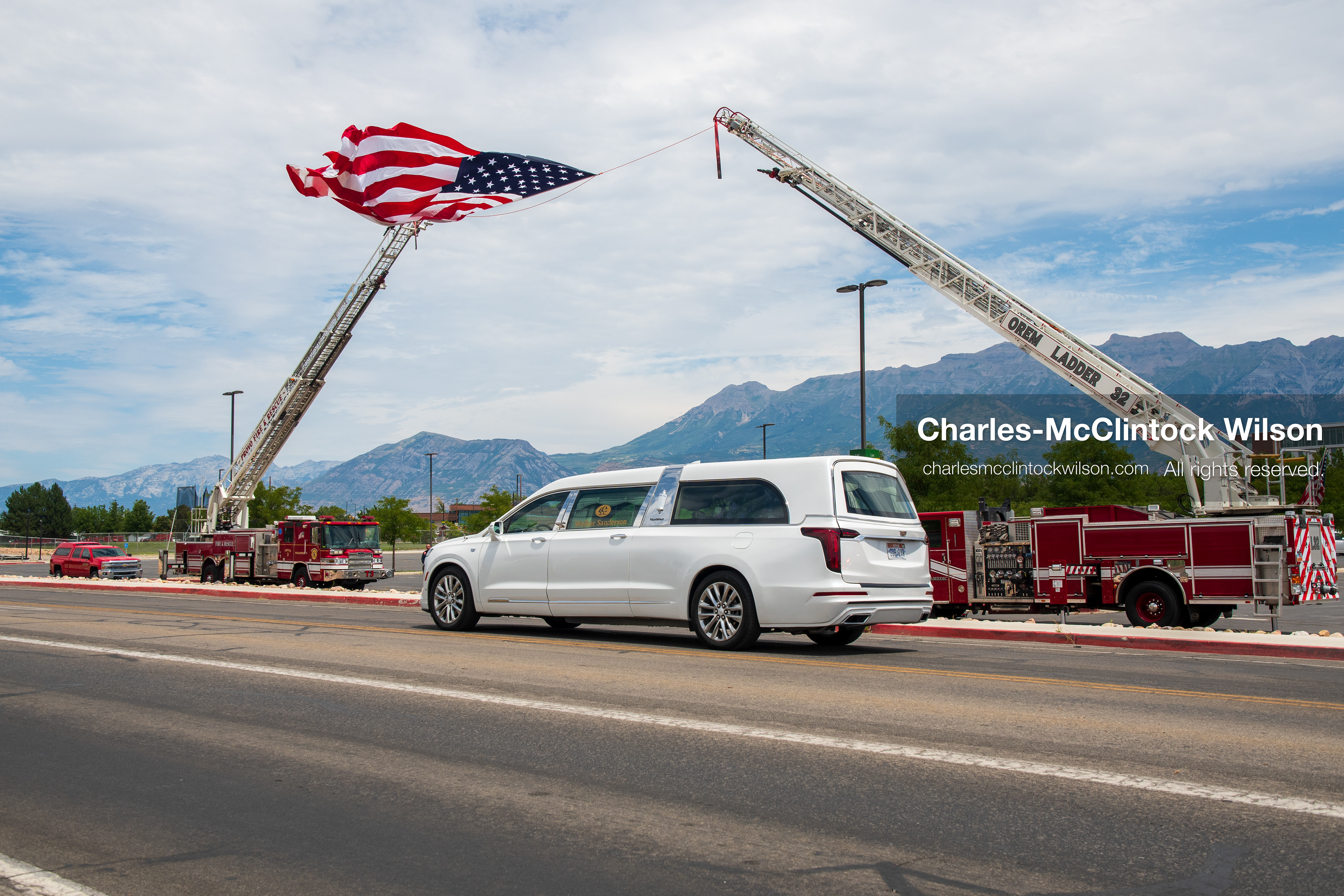 A white Cadillac hearse drives past a massive American flag suspended between two extended fire department ladder trucks during a funeral procession for Provo Fire Captain Spencer Long and his family in Orem, Utah, on Wednesday, July 29, 2026. More than 300 people came to the public memorial ceremony to honor the five family members who died after a flash flood hit their campsite near the Sunglow Campground in Wayne County. (Photo by Charles-McClintock Wilson/Sipa USA)