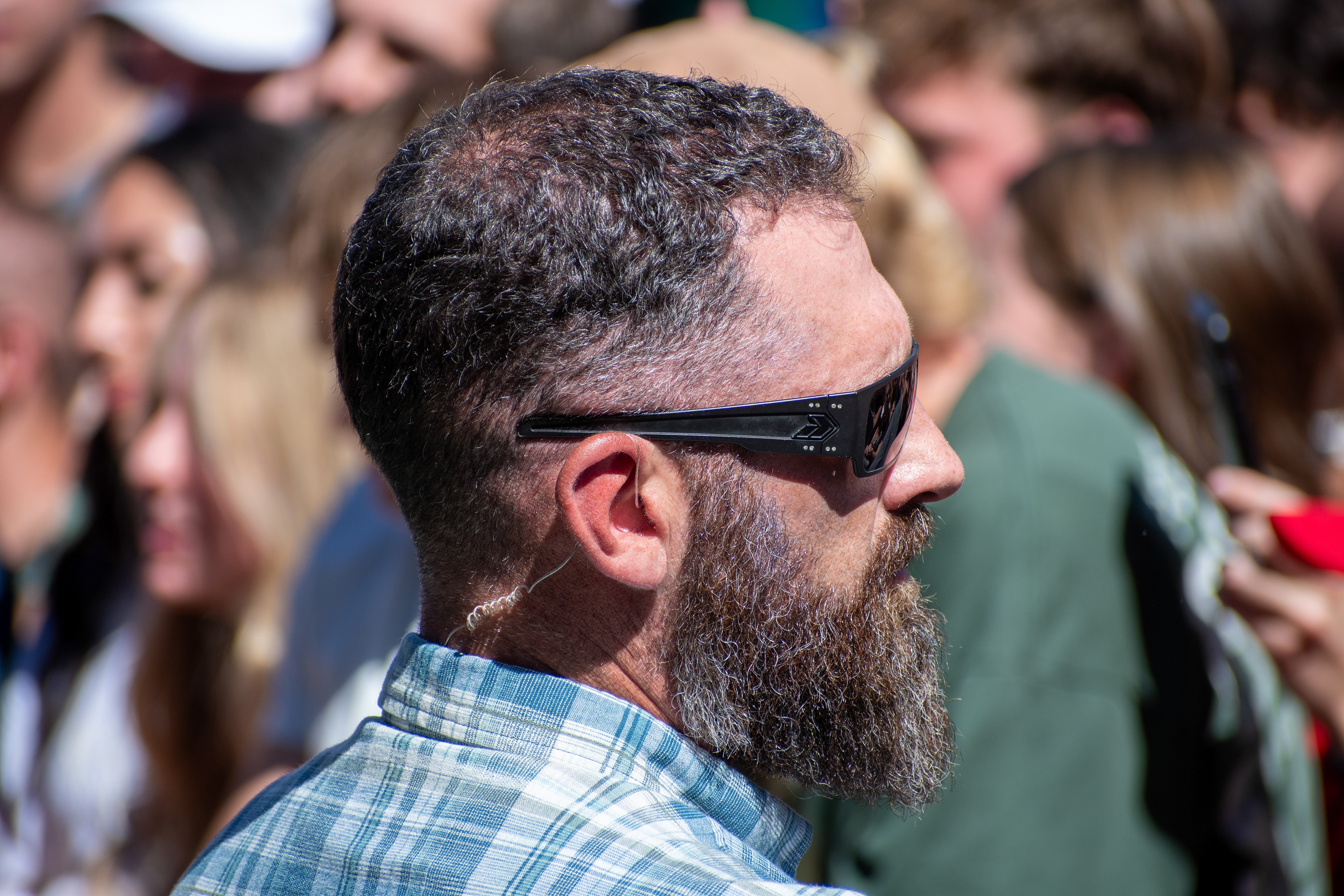 OREM, UTAH – SEPTEMBER 10, 2025: A security detail stands near the perimeter at Utah Valley University during the opening stop of the American Comeback Tour. Positioned beside the crowd, the individual reflects the quiet vigilance and logistical coordination that shaped the event’s atmosphere. The image captures a moment of presence, contrast, and civic anticipation. © Charles-McClintock Wilson / ZUMA Press