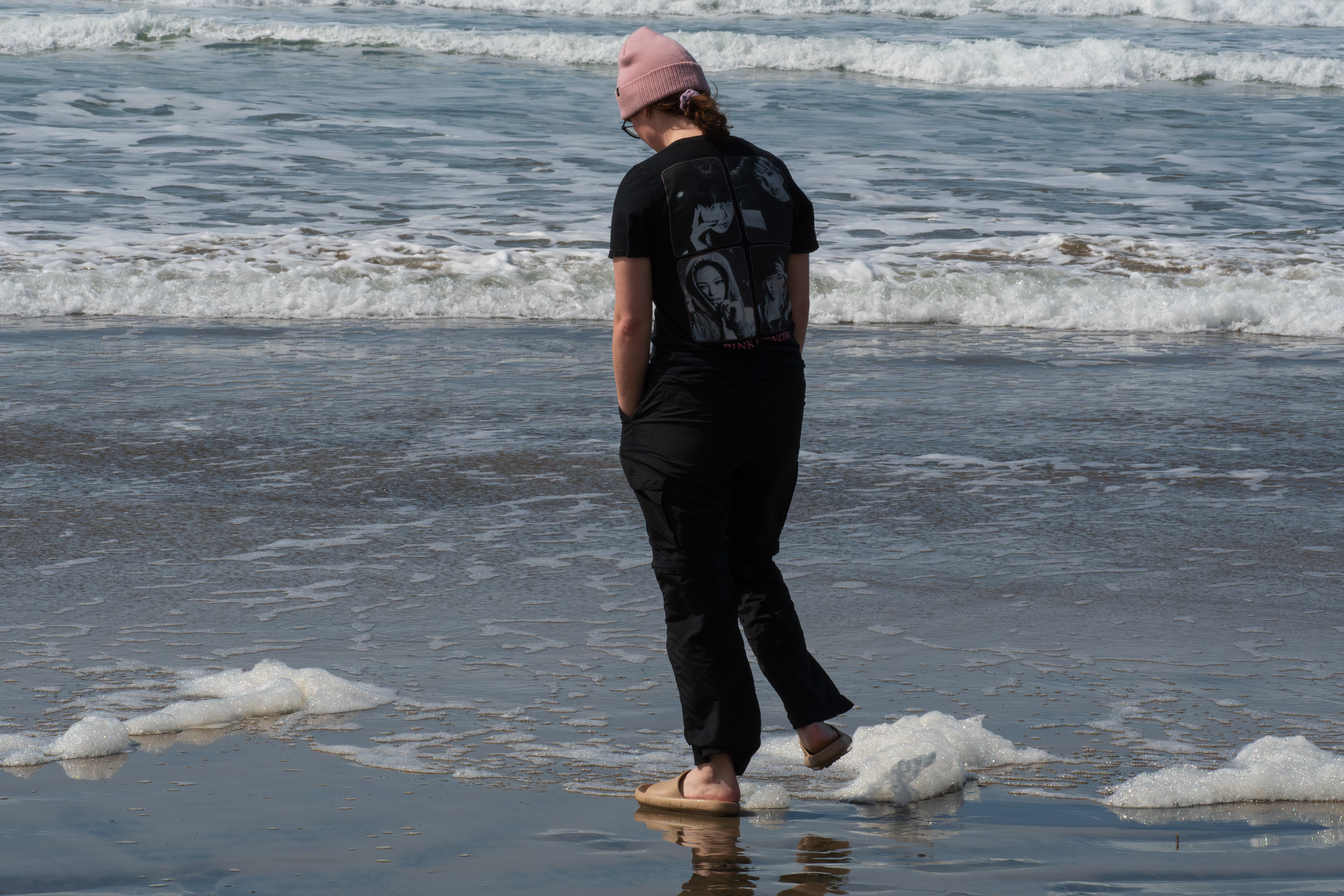 CANNON BEACH, OR - APRIL 12: A young woman walks through reflective surf foam along the shoreline at Cannon Beach on April 12, 2025, in Cannon Beach, Oregon. Spring weather brought clear skies and mild temperatures to the Oregon coast, attracting visitors to its scenic beaches.