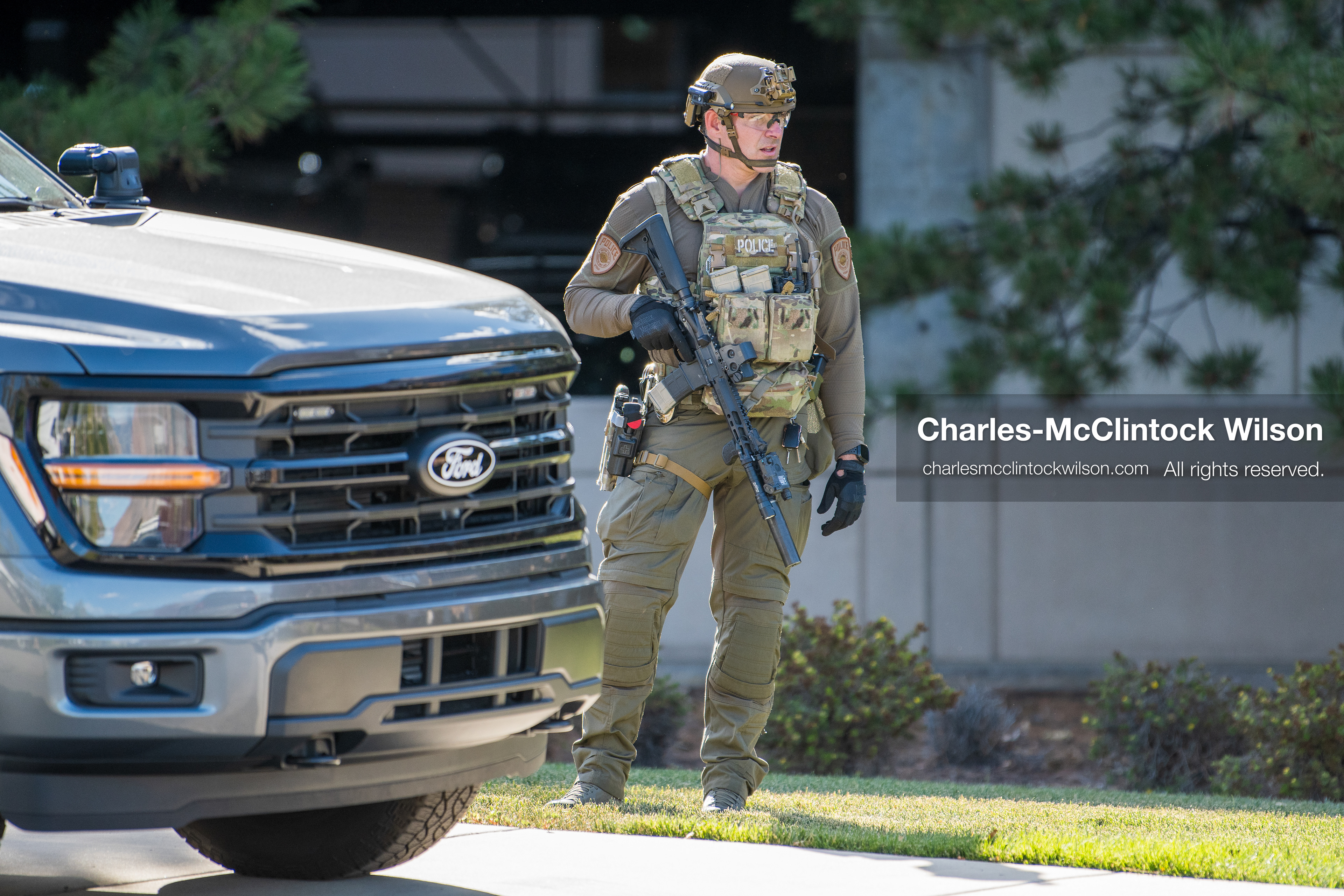 An armed law enforcement officer wearing a helmet and tactical gear stands guard outside Intermountain Medical Center in Murray, Utah, on Monday, August 17, 2026. Multiple regional law enforcement agencies converged to heavily secure the hospital perimeter as a safety precaution after shooting victims arrived from a fatal shootout that erupted outside a funeral service in nearby Kearns earlier that day. (Photo by Charles-McClintock Wilson/Sipa USA)
