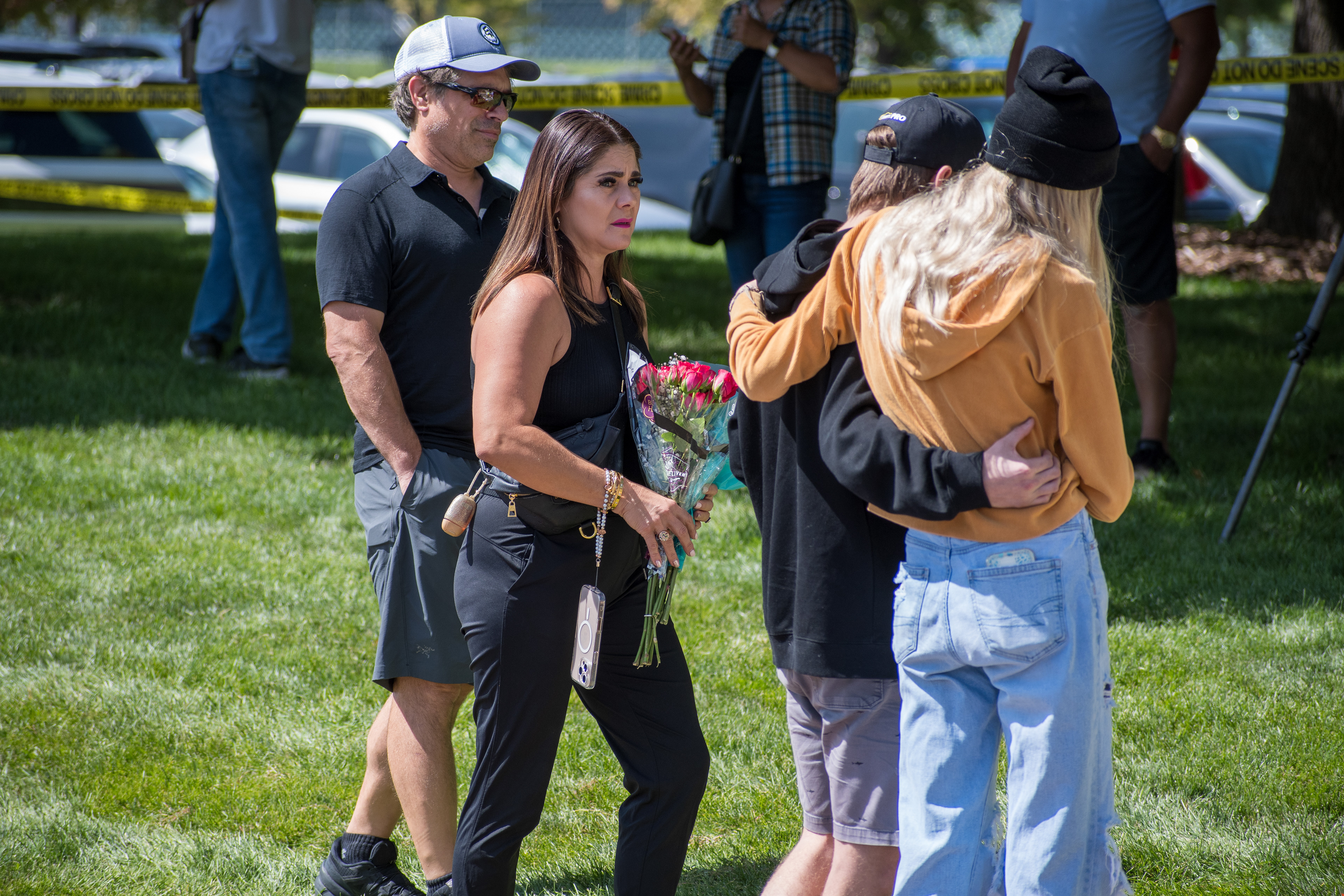 OREM, UTAH – SEPTEMBER 12, 2025: A woman holds a bouquet of red roses as mourners gather at a memorial site for Charlie Kirk near Utah Valley University. In the background, two individuals embrace while others document the scene, reflecting a moment of solemn remembrance. © Charles‑McClintock Wilson / ZUMA Press