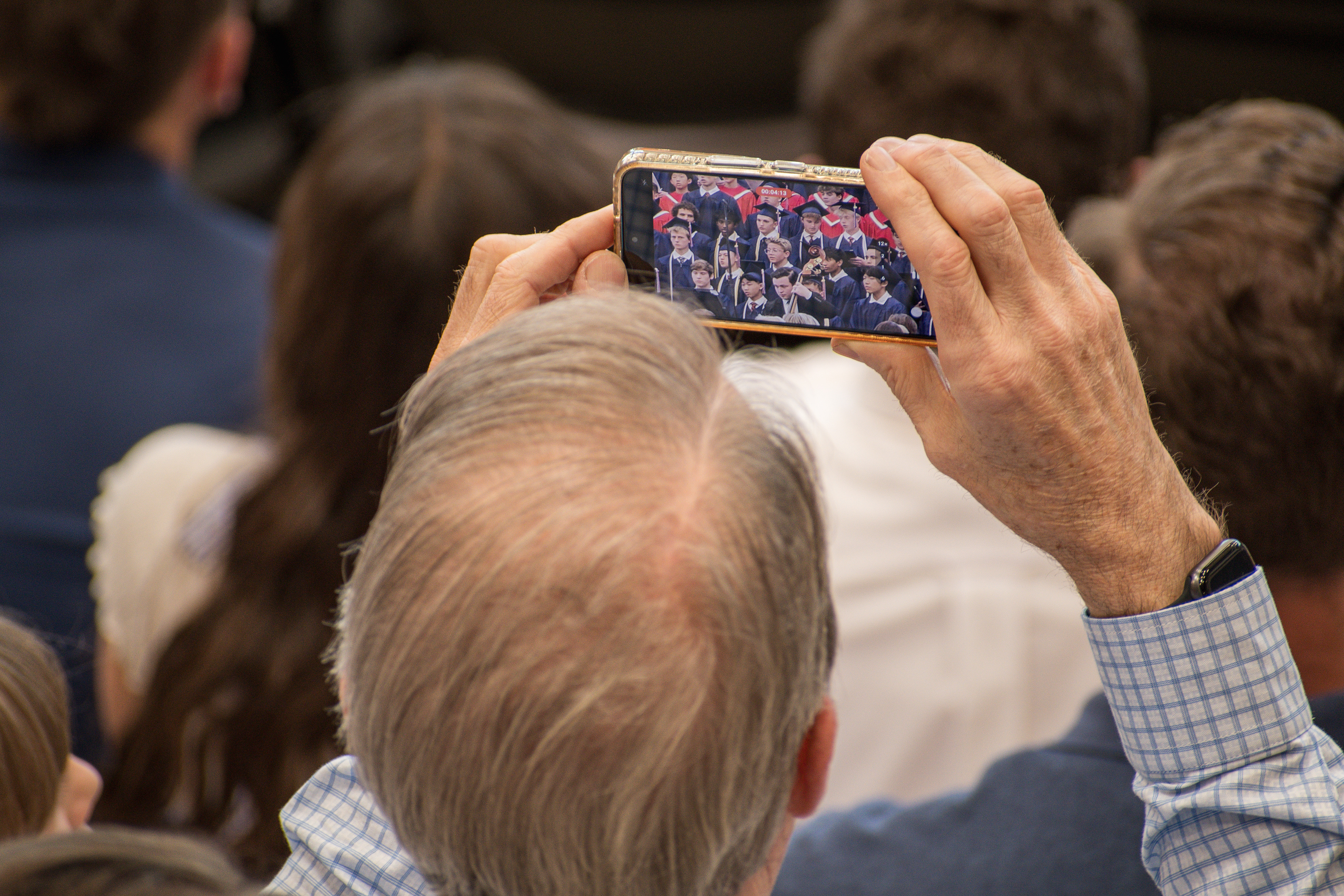 American Fork, UT, USA – May 24, 2025: A man uses his smartphone to record a graduation ceremony at an academy in American Fork, Utah.